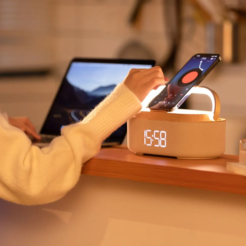 Osoba z telefonem na drewnianym urządzeniu z zegarem i laptopem w tle.