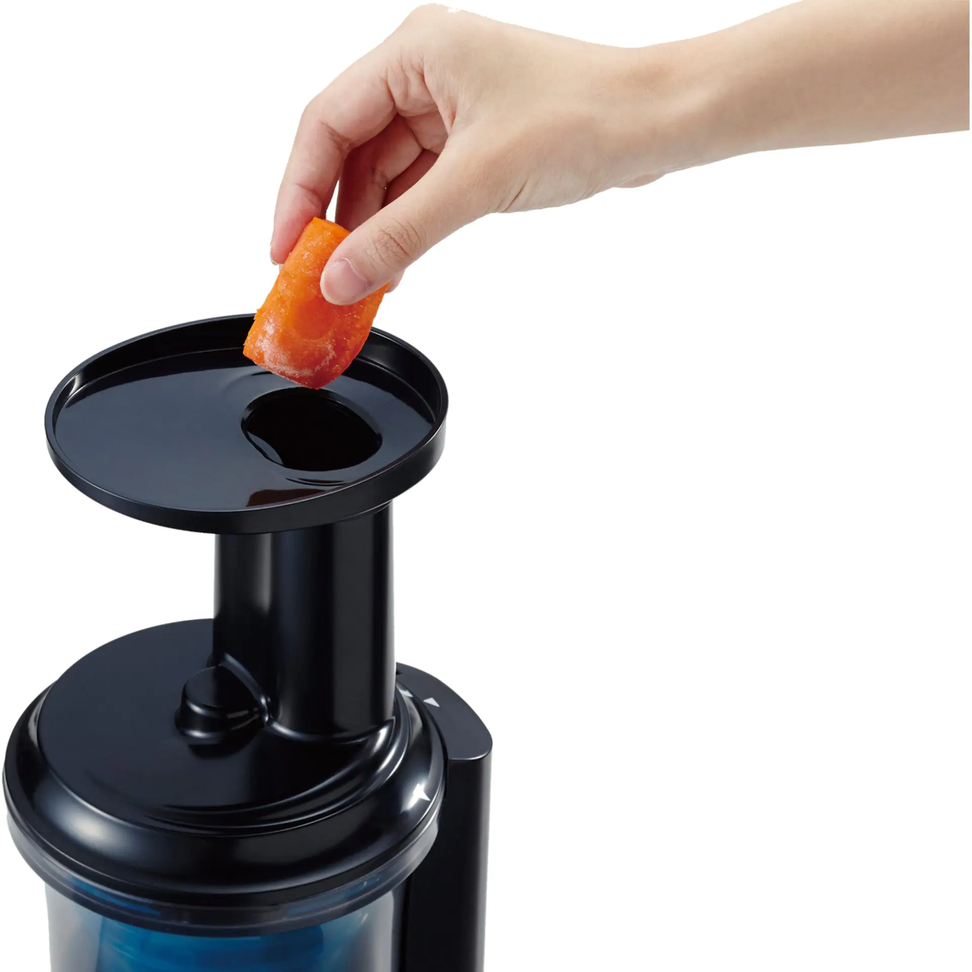 Ręka wkładająca kawałek marchwi do czarnej wyciskarki.