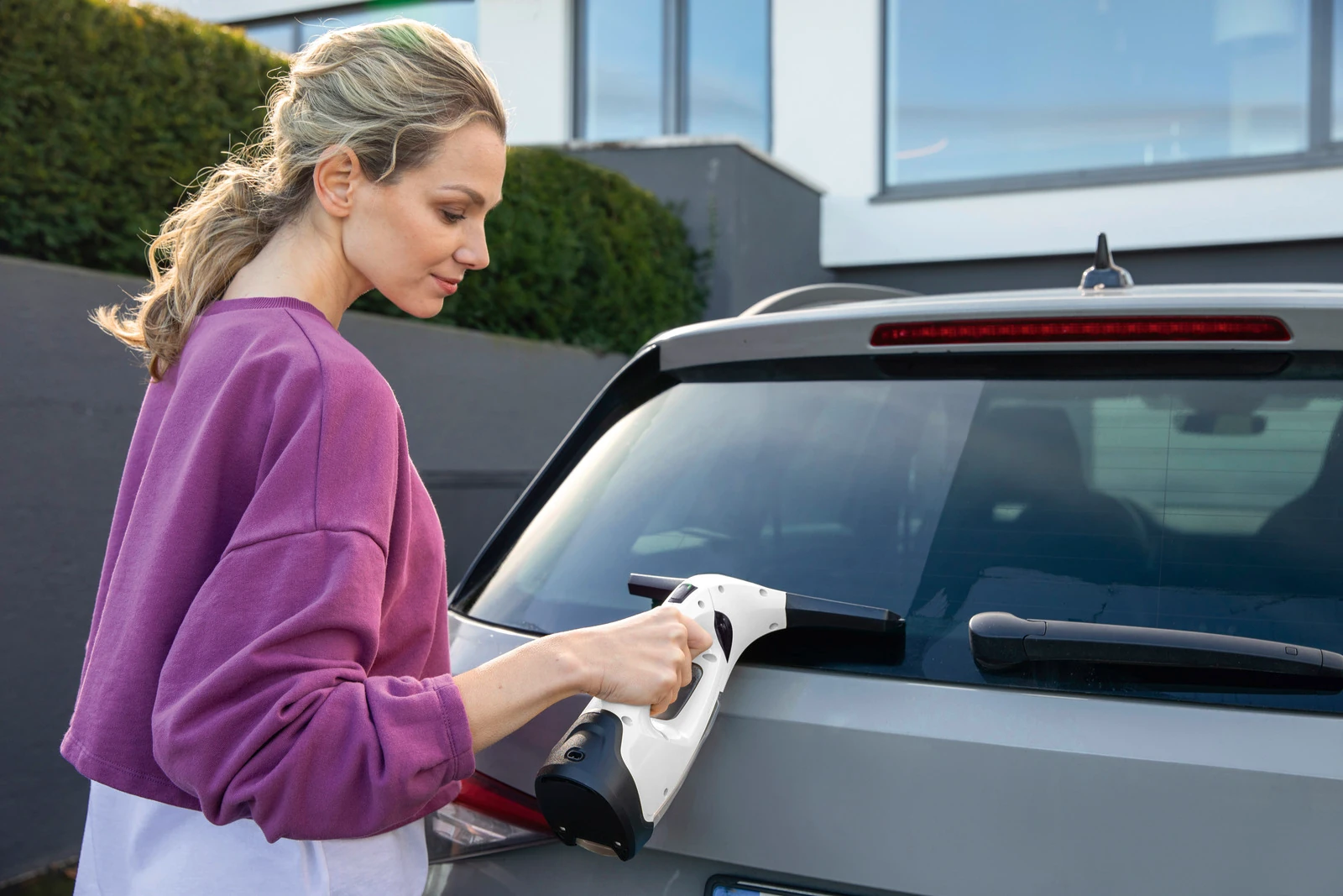 Kobieta czyści szybę samochodu za pomocą środka czyszczącego.