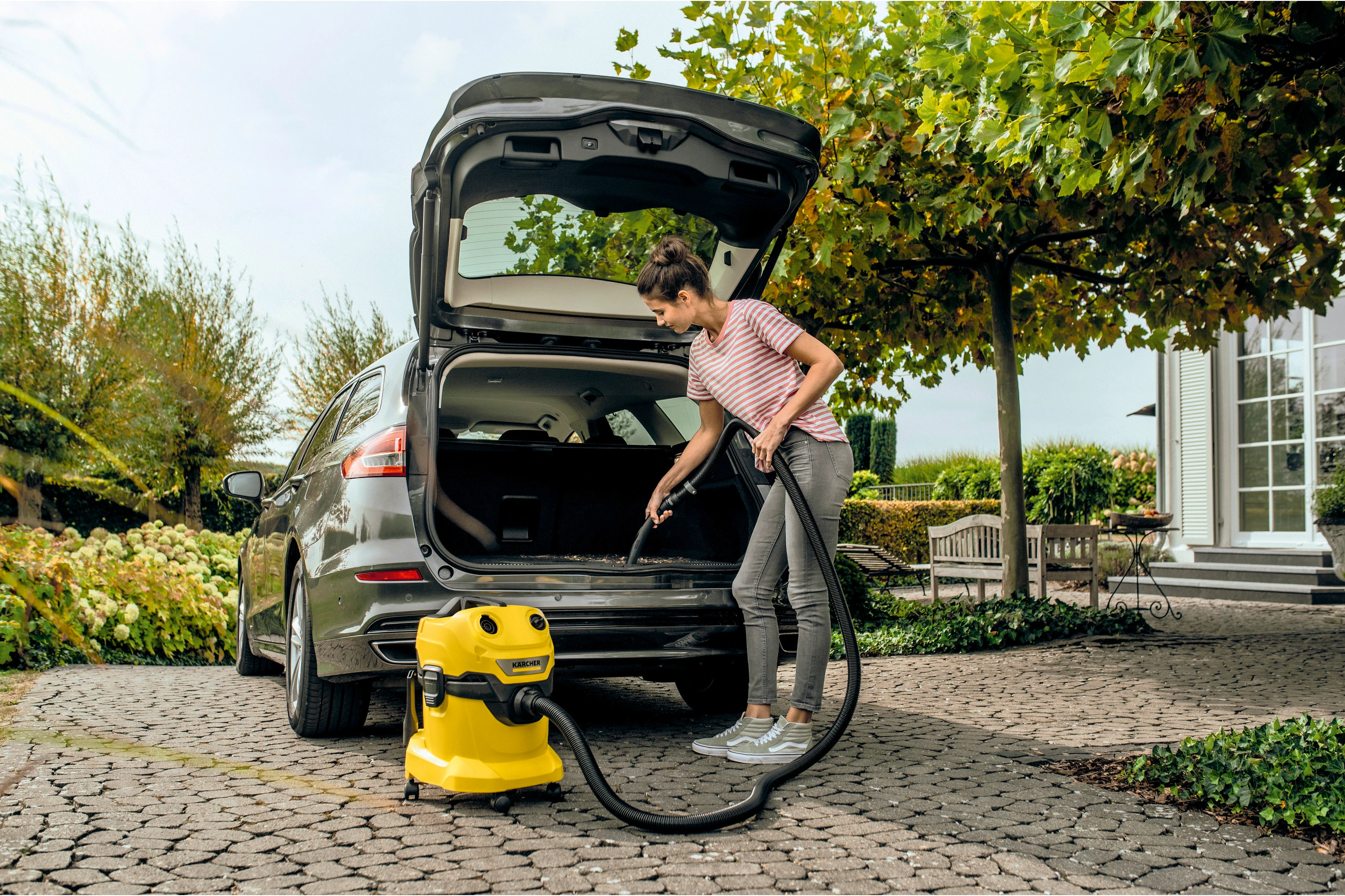 Kobieta odkurzająca bagażnik samochodu żółtym odkurzaczem.