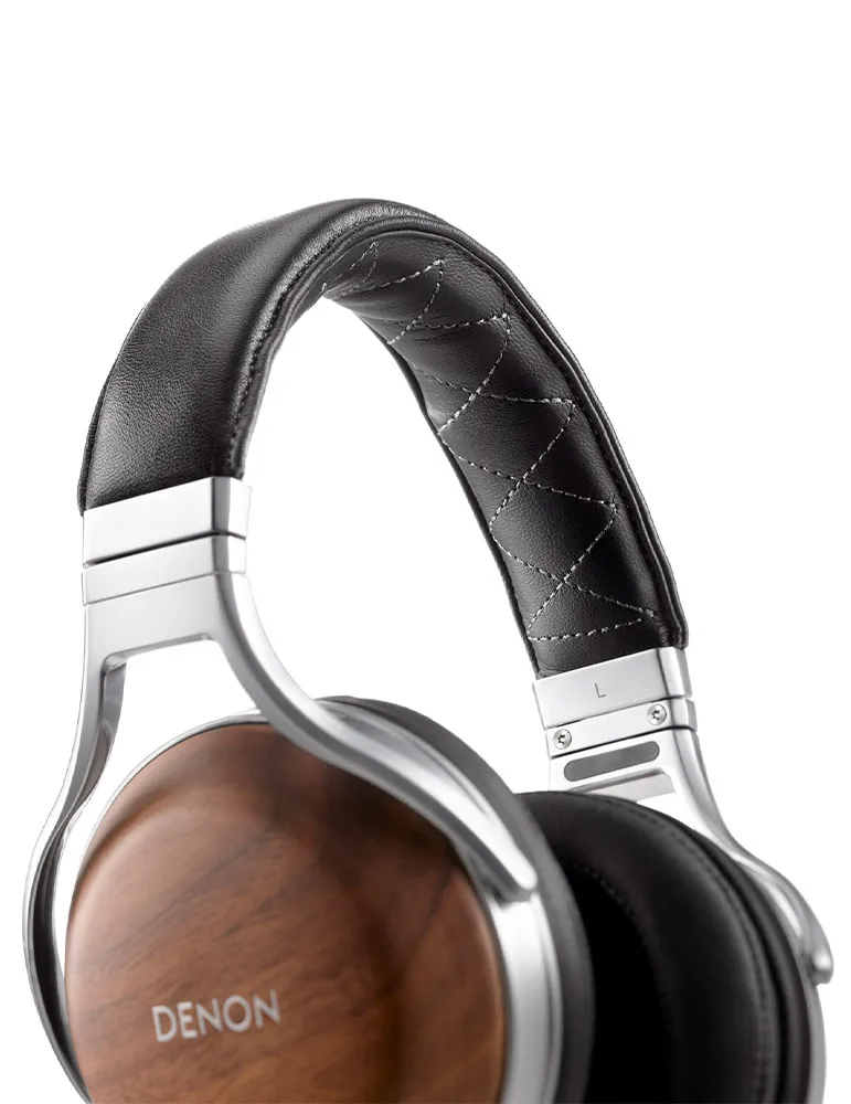 Zbliżenie słuchawek Denon. Czarny skórzany pałąk z przeszyciami, srebrna rama, drewniane nauszniki. Białe tło.