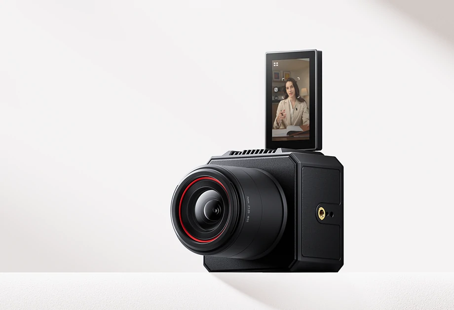 Czarny aparat z obiektywem i ekranem pokazującym kobietę. Aparat stoi na białej powierzchni z białym tłem.