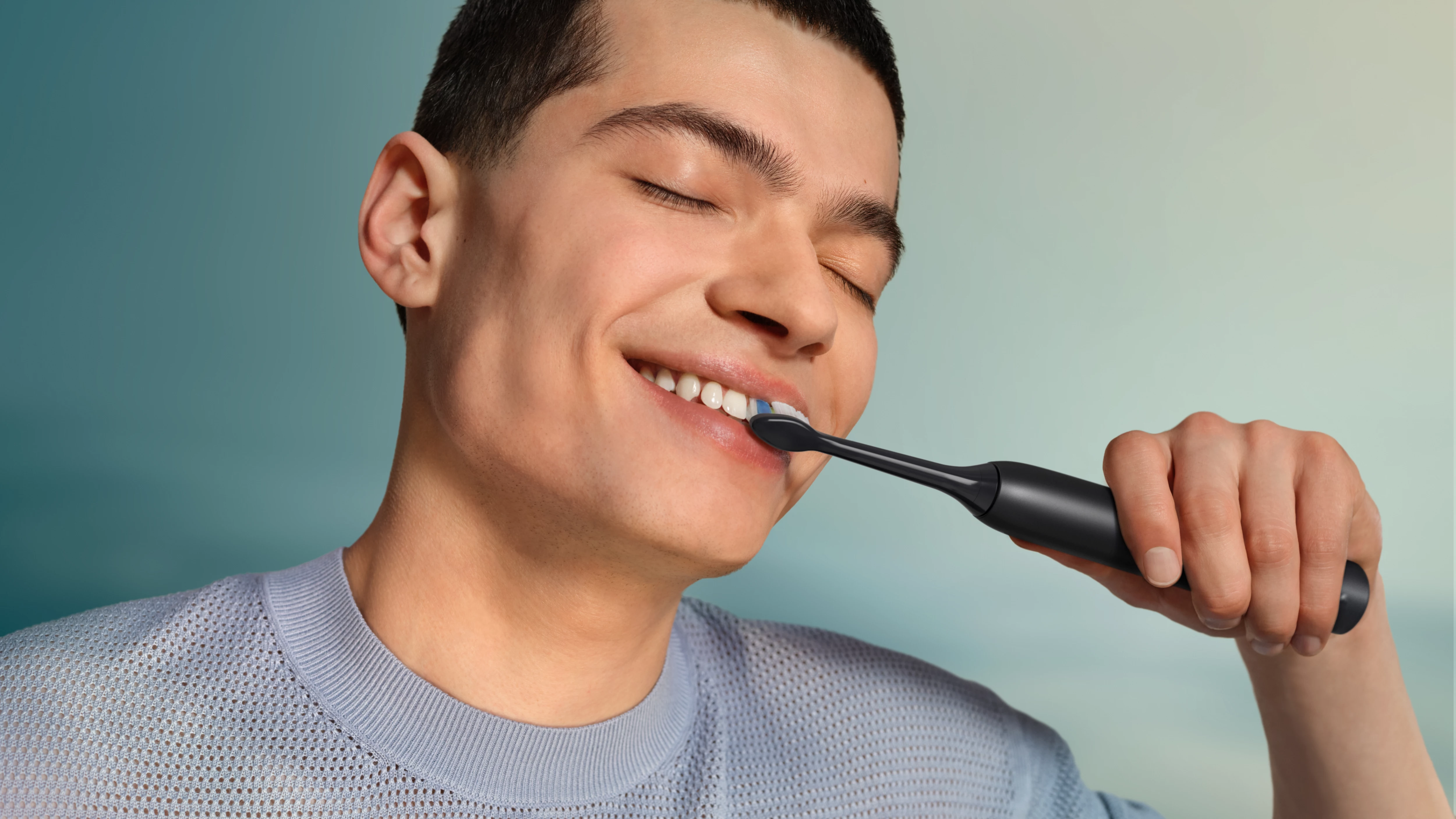 Mężczyzna myje zęby szczoteczką elektryczną na niebieskim tle.