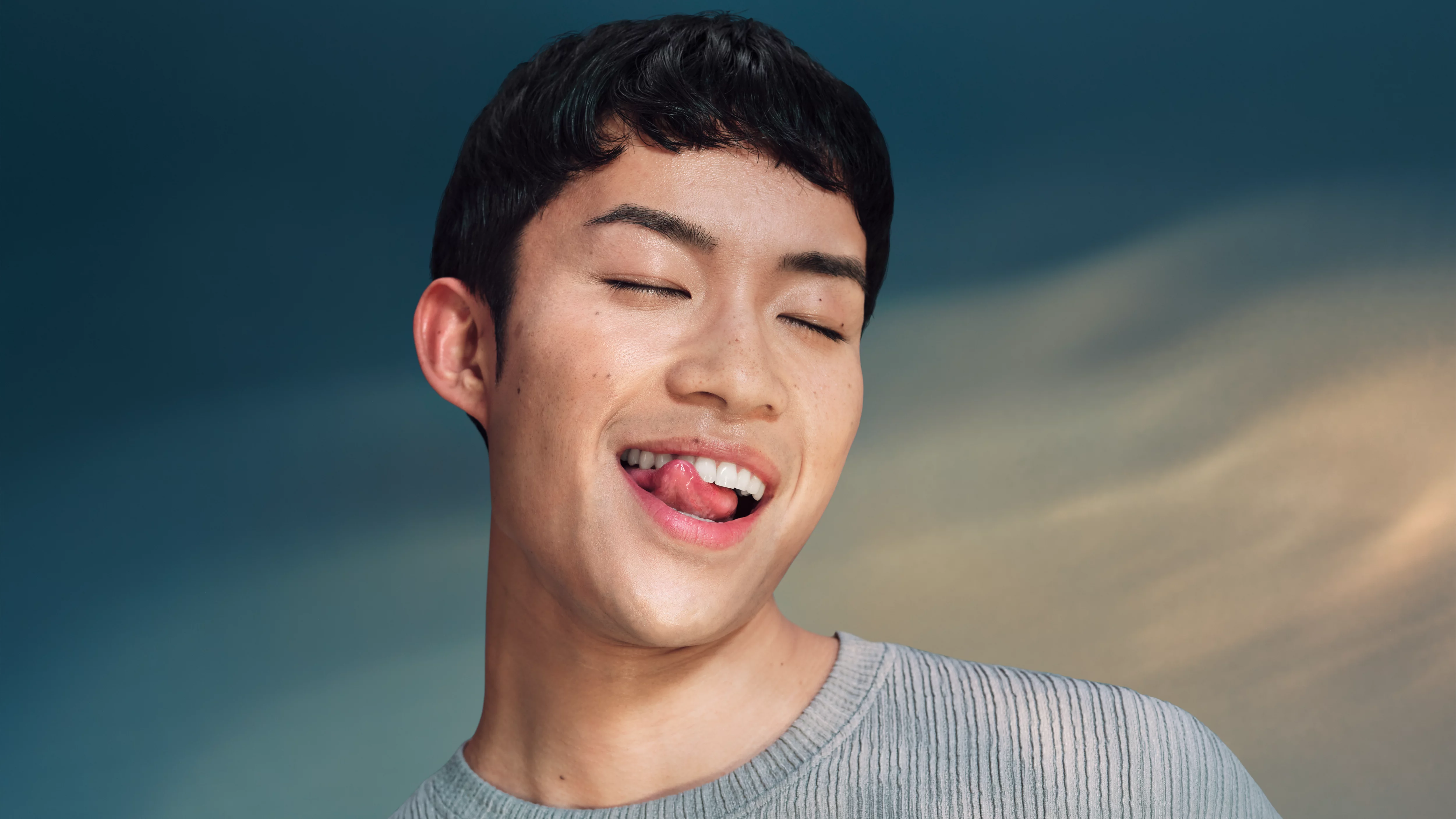 Młody mężczyzna z zamkniętymi oczami liże wargi, na tle błękitnego nieba.