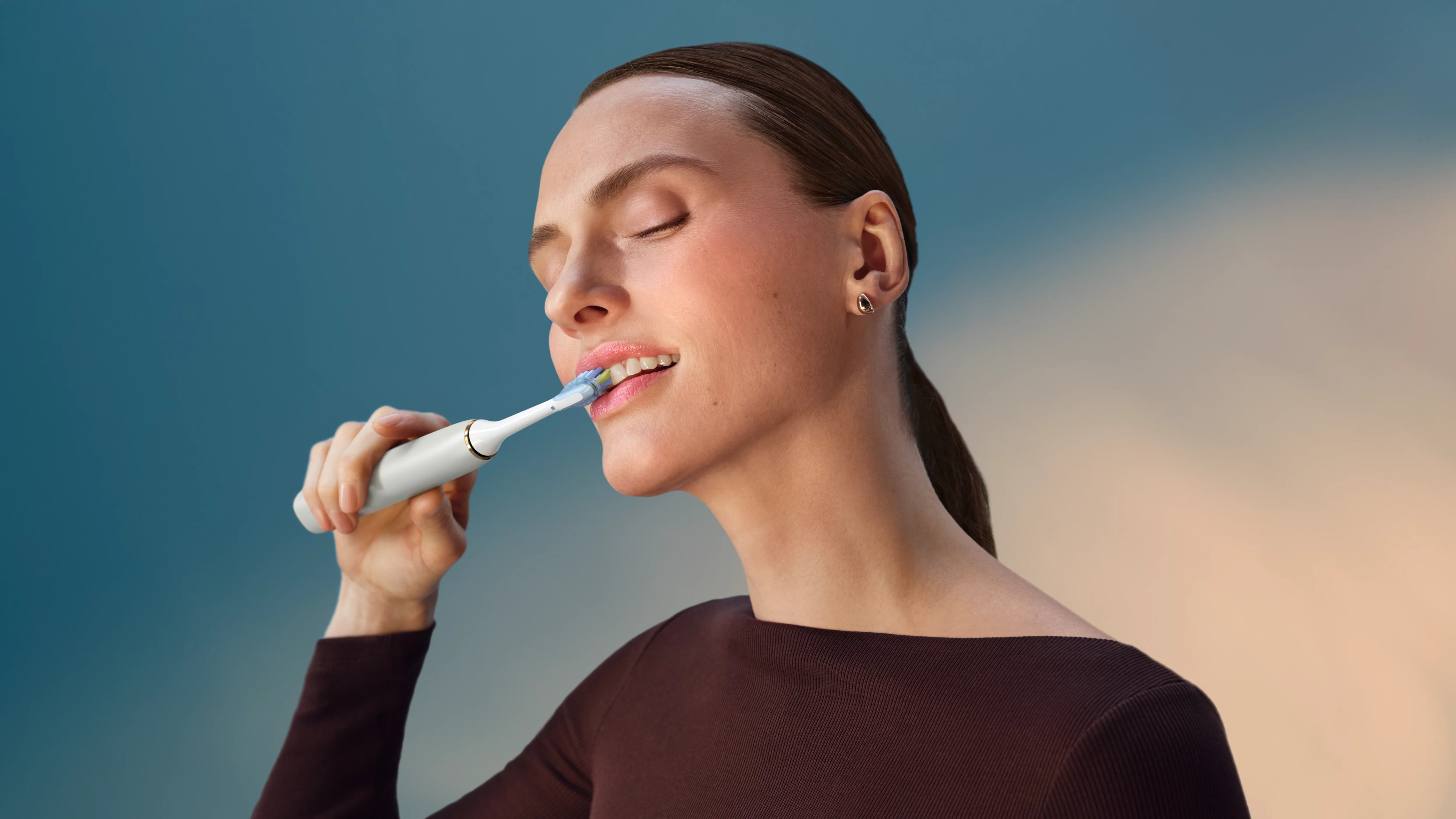 Kobieta myje zęby szczoteczką elektryczną.