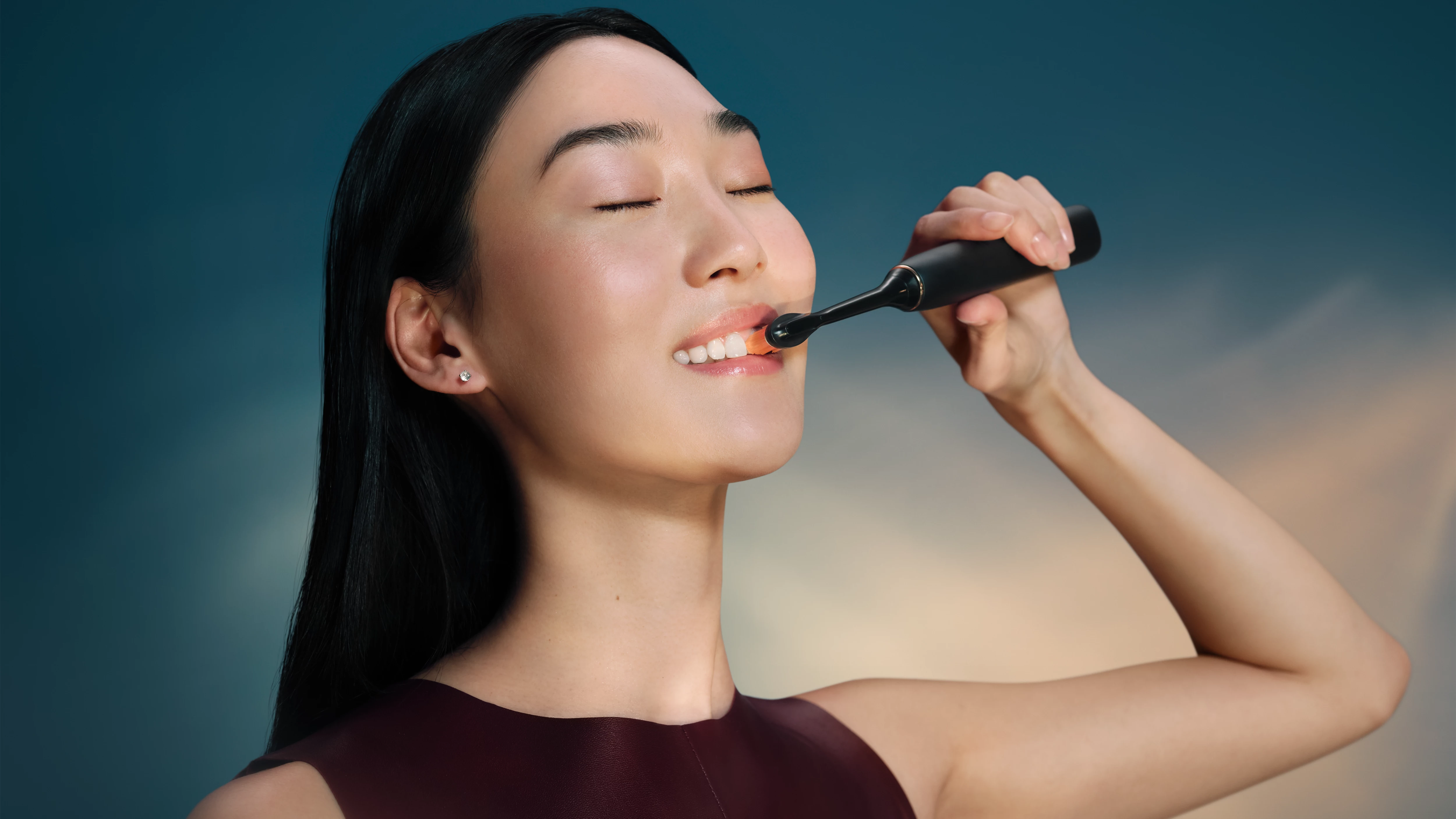 Kobieta myje zęby czarną szczoteczką elektryczną, z zamkniętymi oczami.