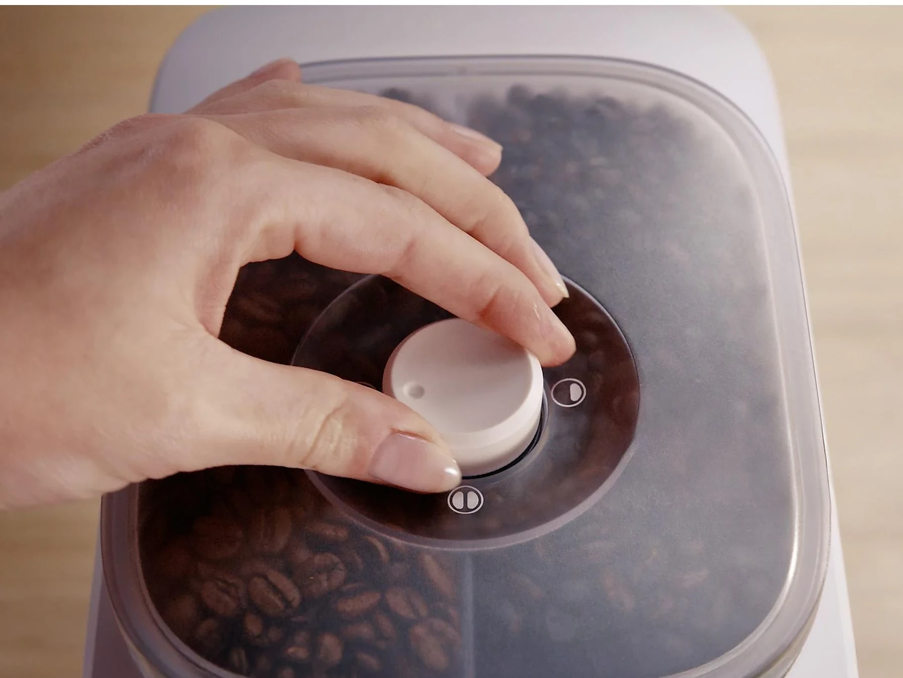 Ręka przekręca pokrętło na pojemniku z ziarnami kawy.