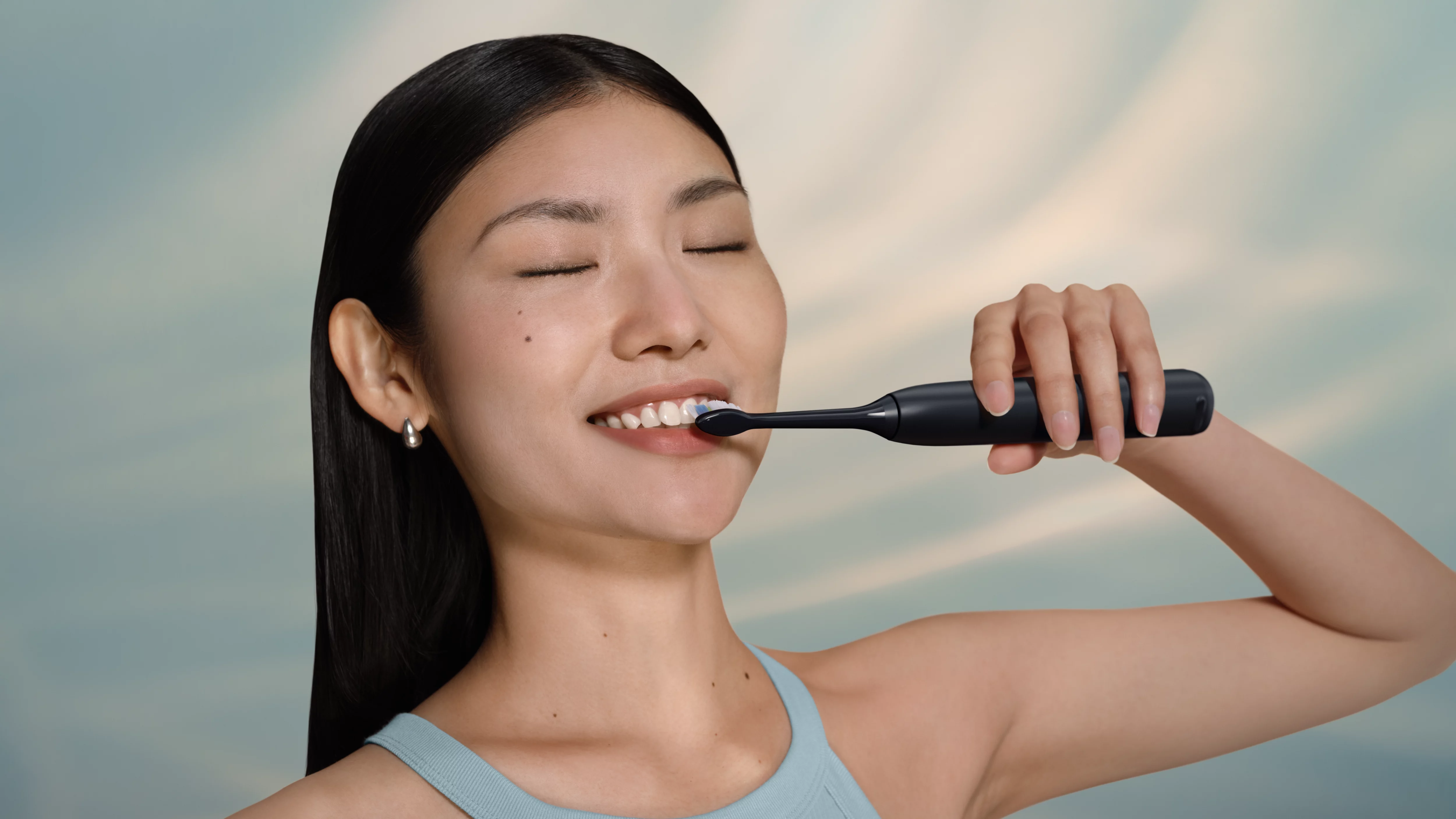 Kobieta myje zęby czarną szczoteczką elektryczną.