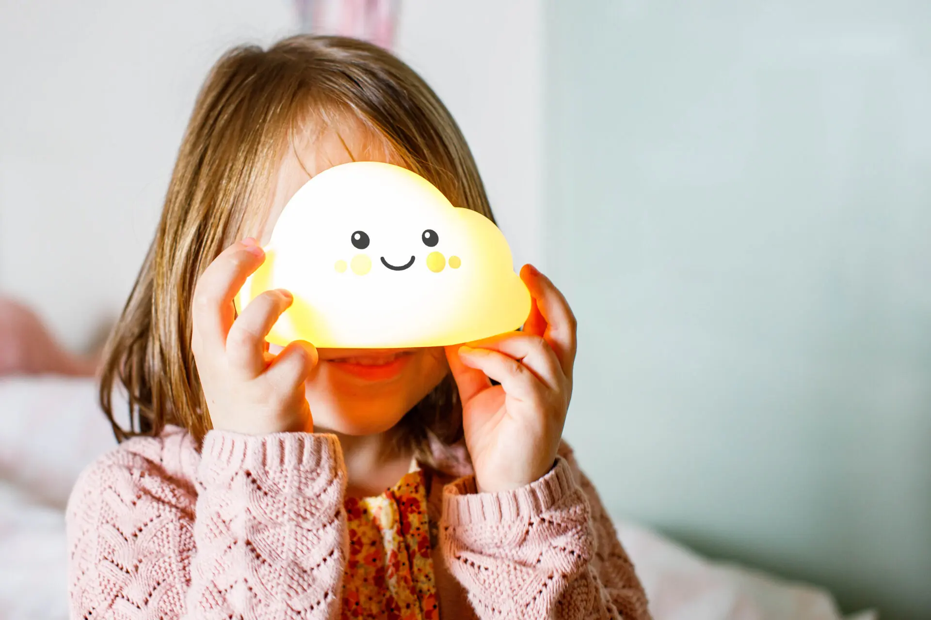 Mała dziewczynka trzymająca świecącą lampkę chmurkę przed twarzą.