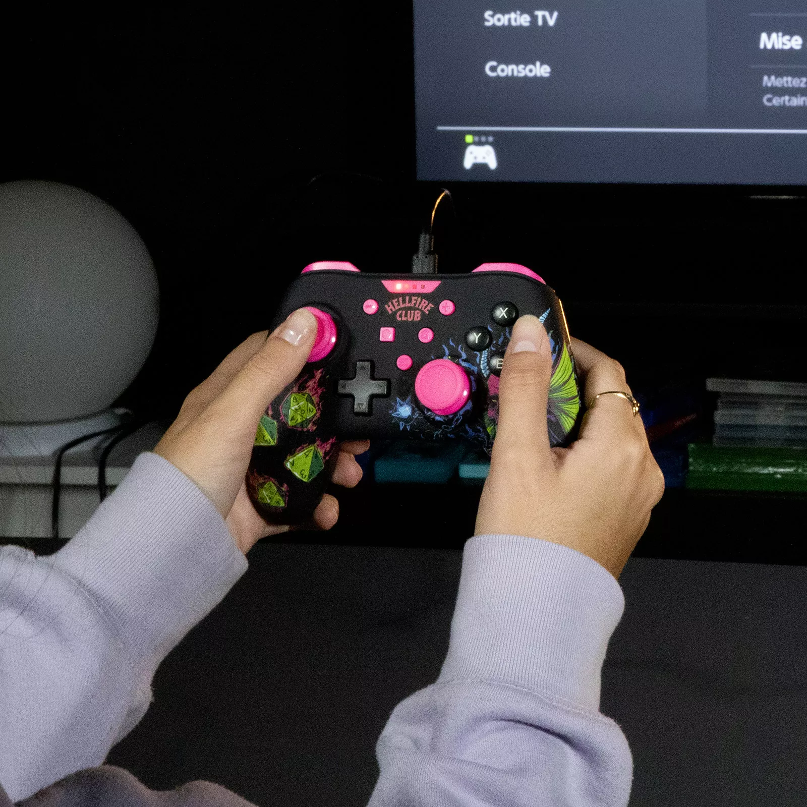Dłonie trzymające czarny kontroler do gier z różowymi przyciskami.