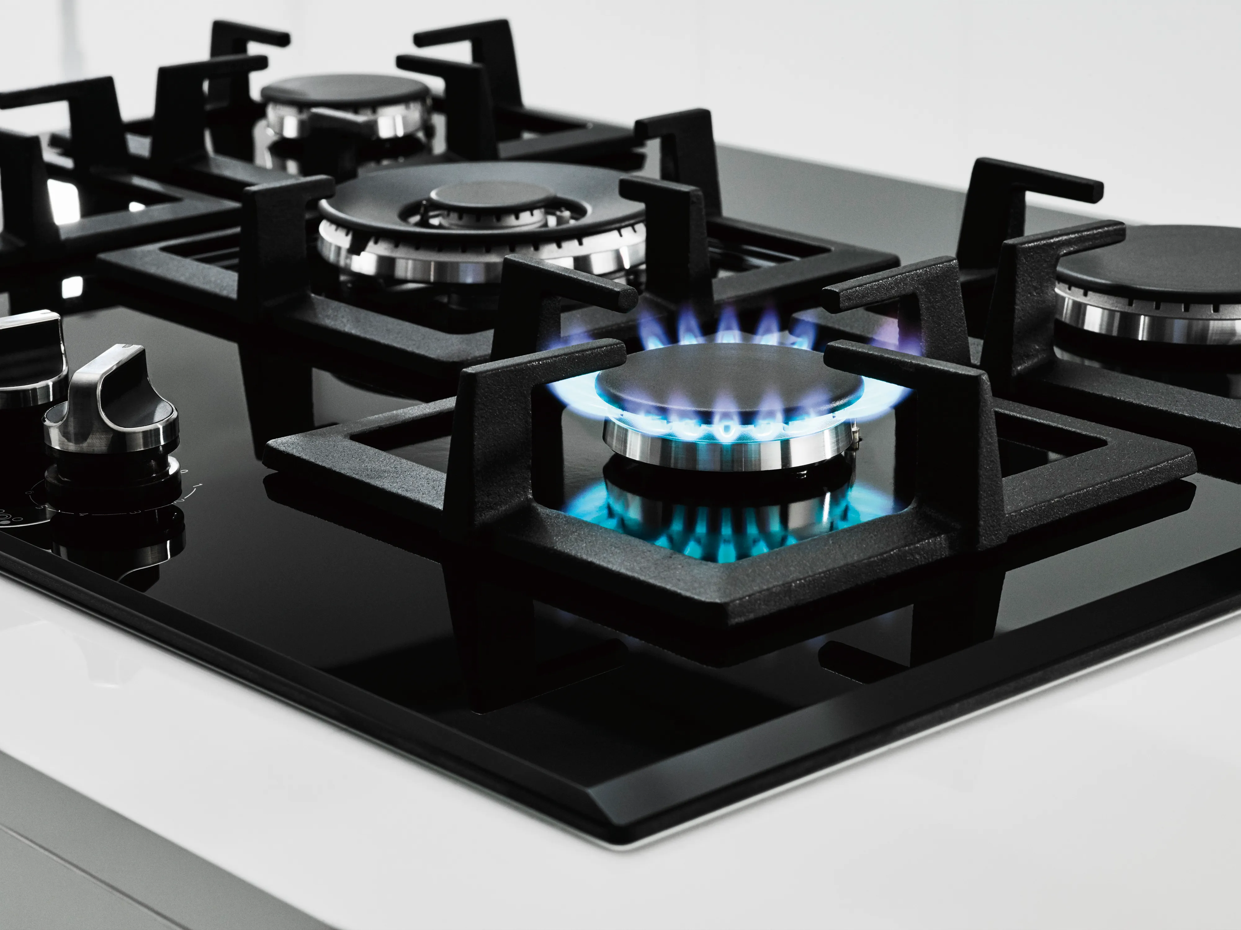 Czarna płyta gazowa z czterema palnikami, z których jeden pali się niebieskim płomieniem.
