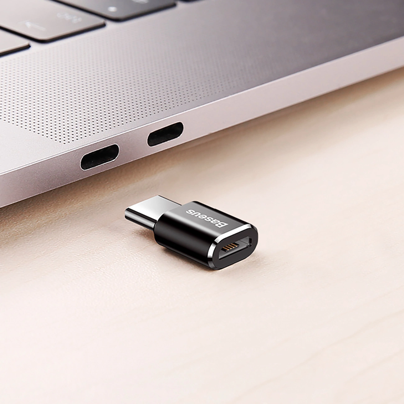 Czarny adapter USB-C obok laptopa. Adapter ma srebrne logo 'Baseus'.