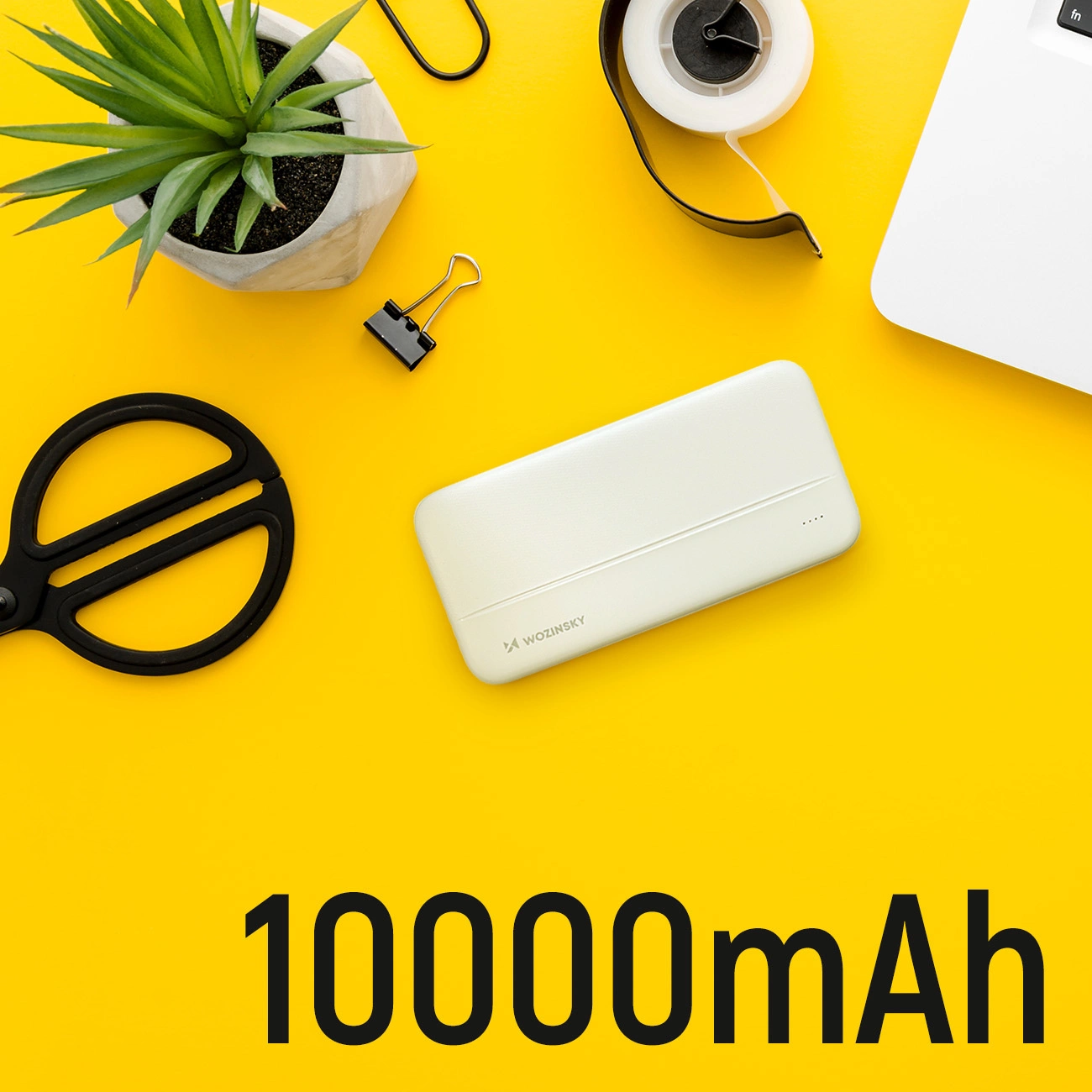Żółte tło z power bankiem, nożyczkami, rośliną, taśmą, spinaczem i laptopem. Tekst: 10000mAh.