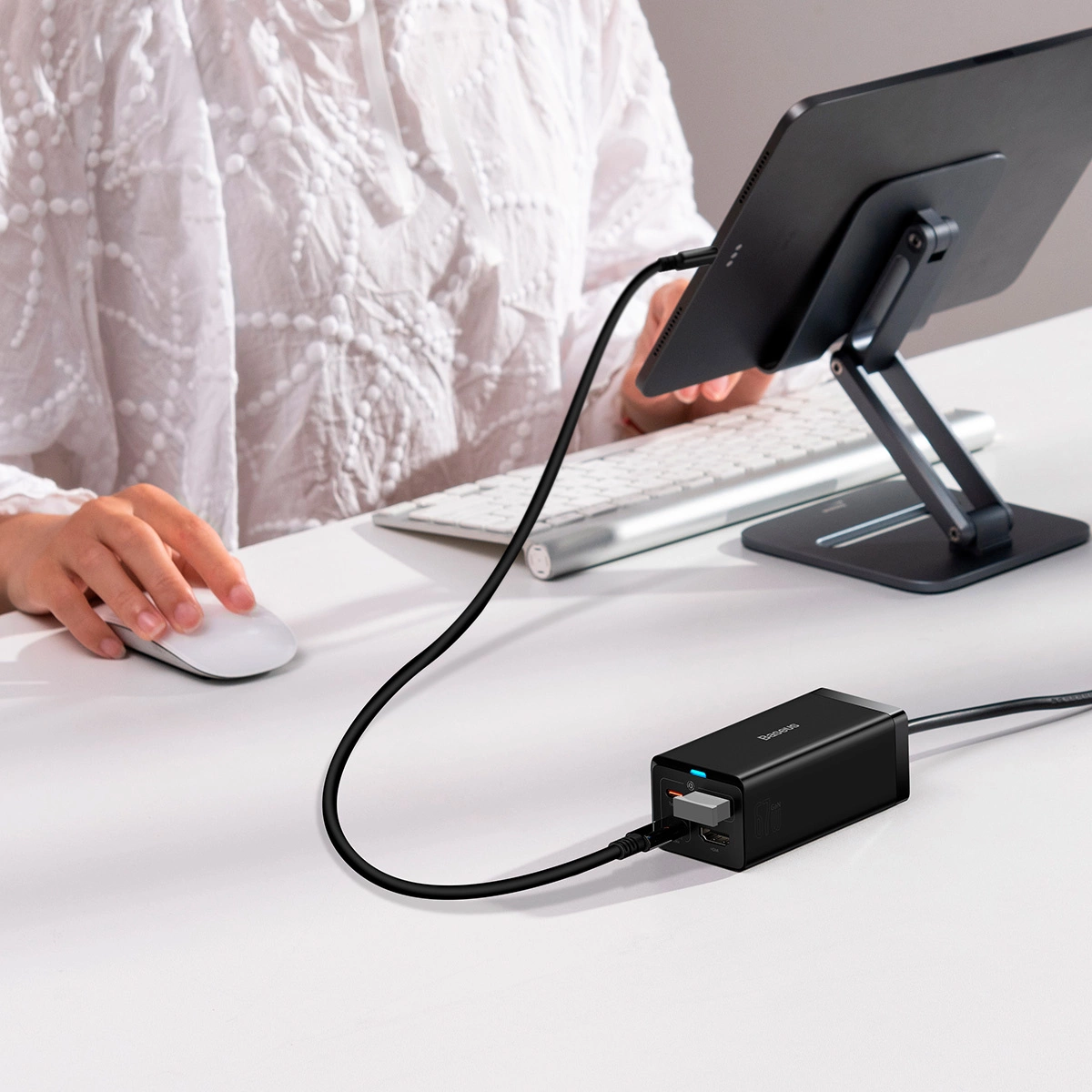 Osoba używa myszy przy biurku z tabletem na stojaku. Czarna ładowarka jest podłączona do tabletu.