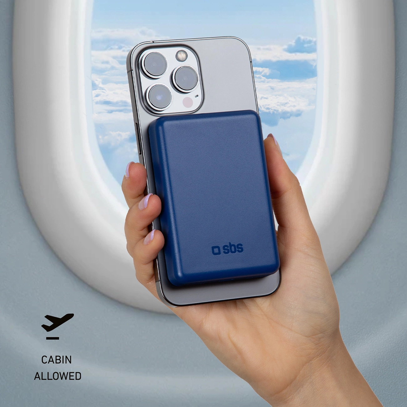 Ręka trzyma telefon z dołączoną niebieską ładowarką. Tło okna samolotu. Logo dozwolone w kabinie.