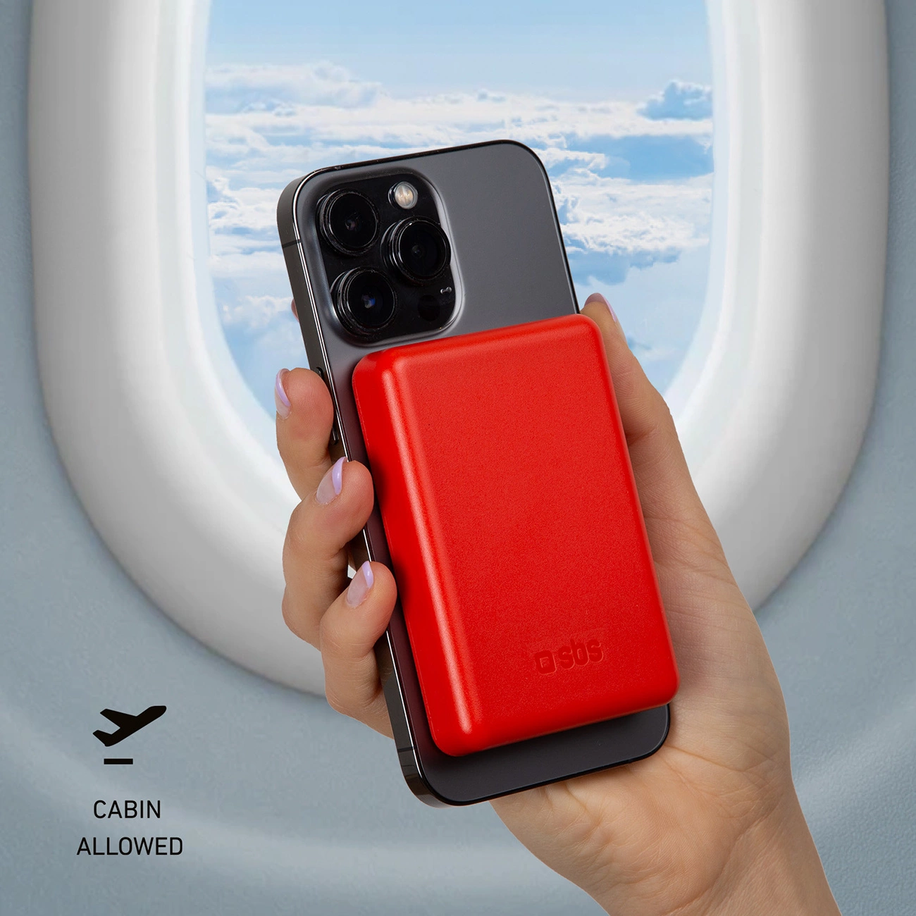 Ręka trzyma telefon z czerwoną power bank. Tło przedstawia okno samolotu z chmurami i ikoną 'Dozwolone w kabinie'.