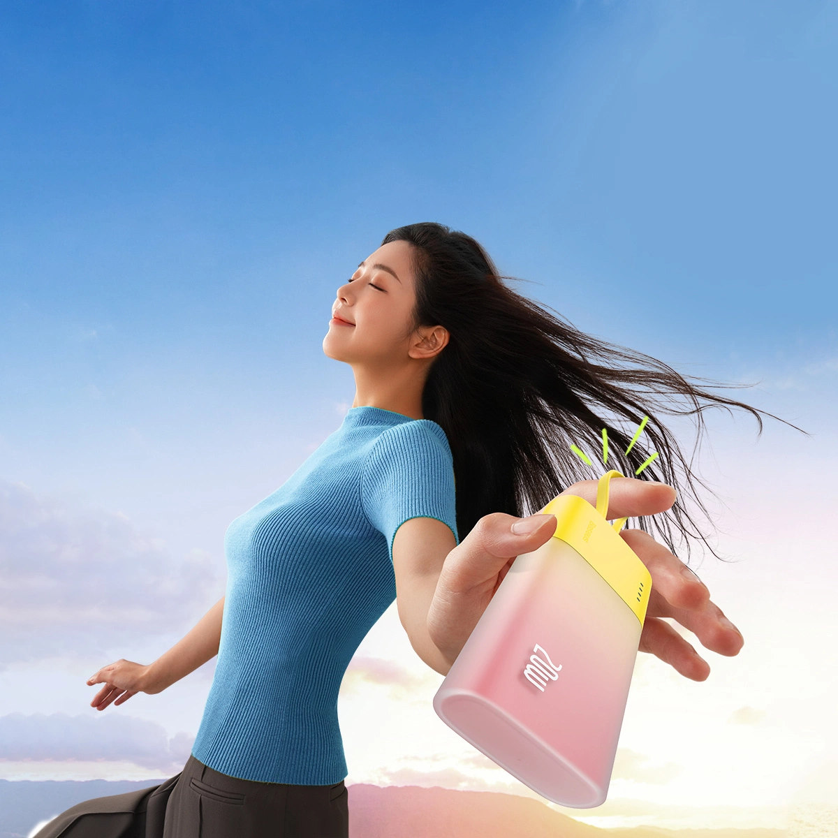 Kobieta trzyma e-papierosa na tle niebieskiego nieba. Ma na sobie niebieską koszulę i ciemne spodnie. E-papieros jest żółty i różowy.