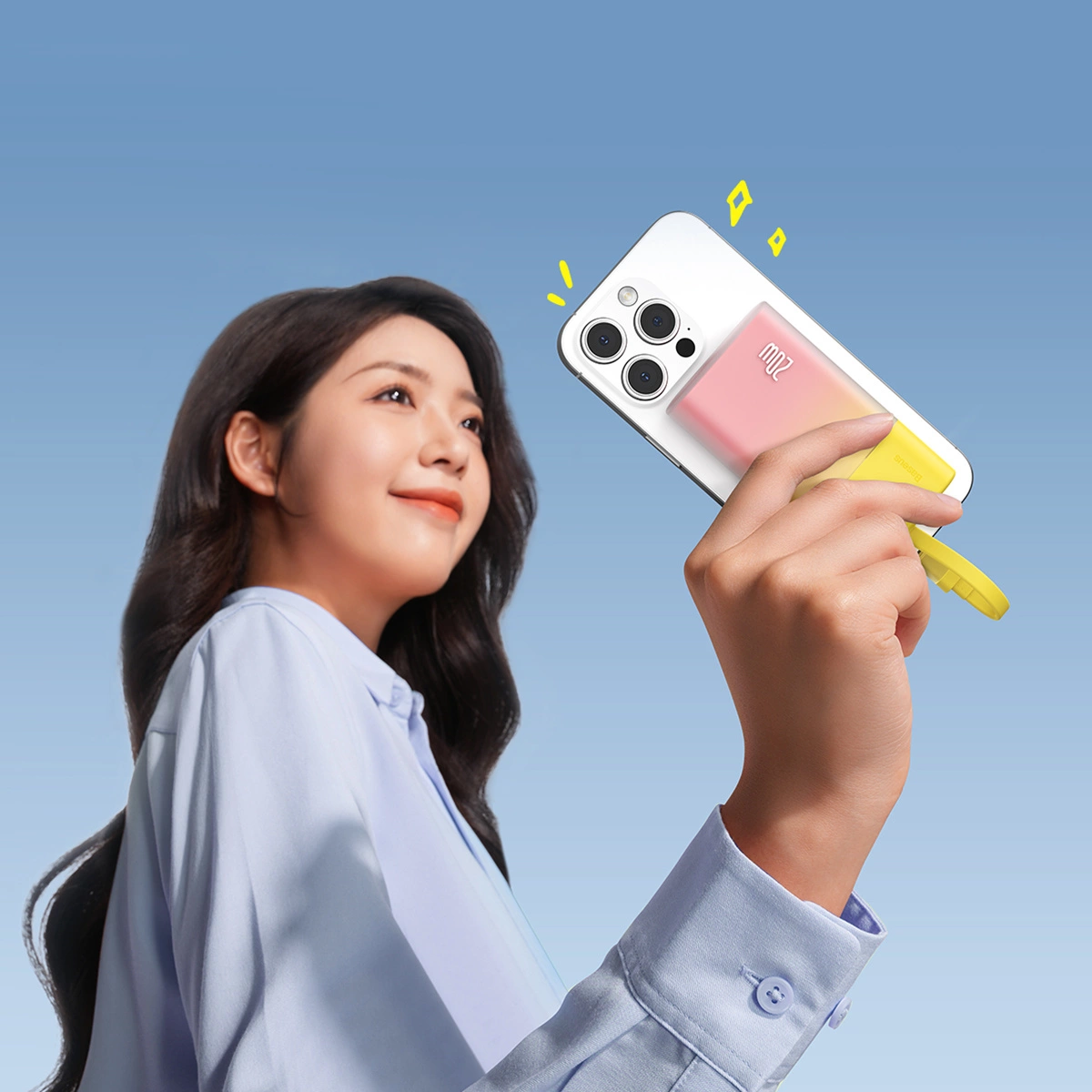 Kobieta trzymająca telefon z ładowarką. Telefon i ładowarka są białe, różowe i żółte. Tło nieba.