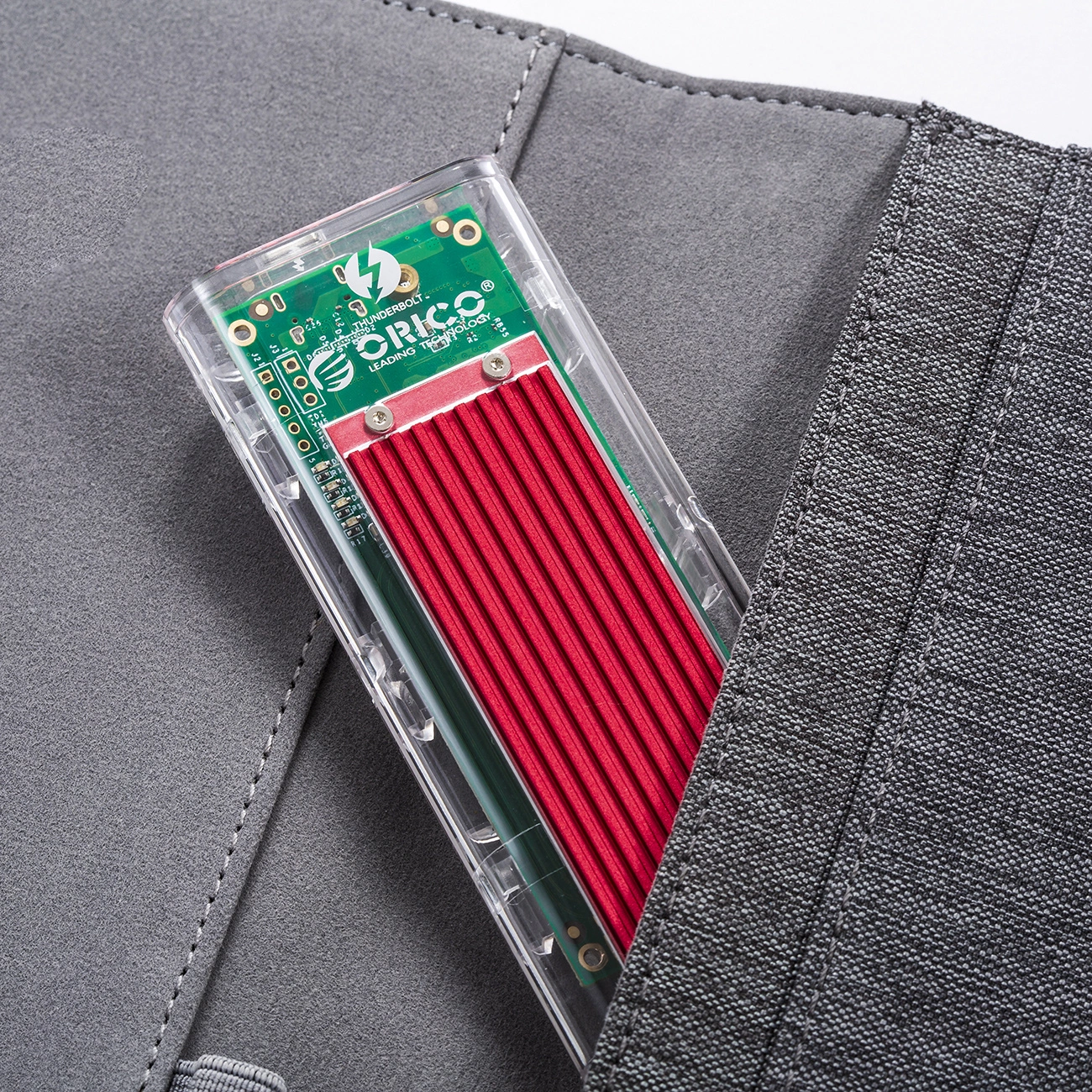 Przezroczysta obudowa z czerwonym elementem i zieloną płytką drukowaną, częściowo w szarej kieszeni.