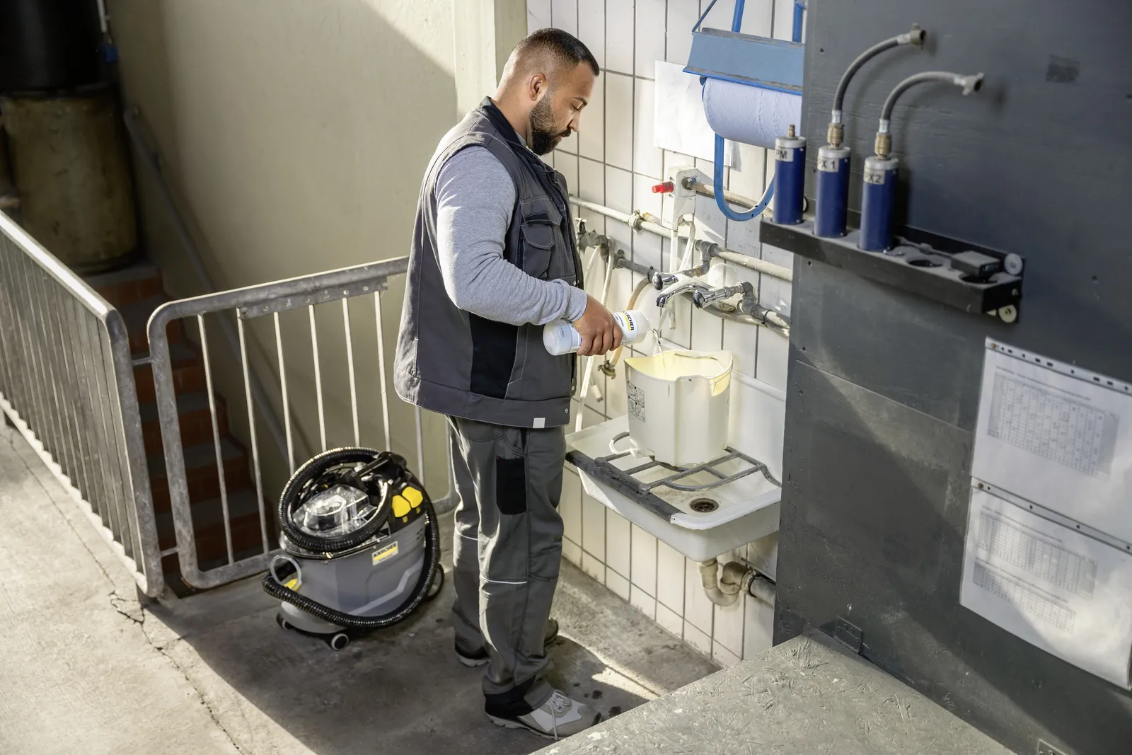 Mężczyzna wlewa płyn z butelki do wiadra pod kranem, w pobliżu środek czyszczący.