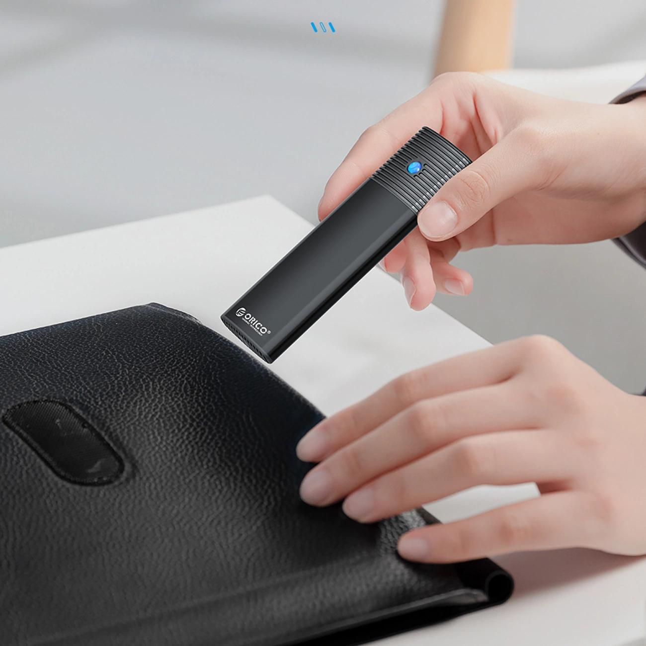 Osoba trzyma czarny dysk ORICO z niebieskim światłem nad czarnym folderem.