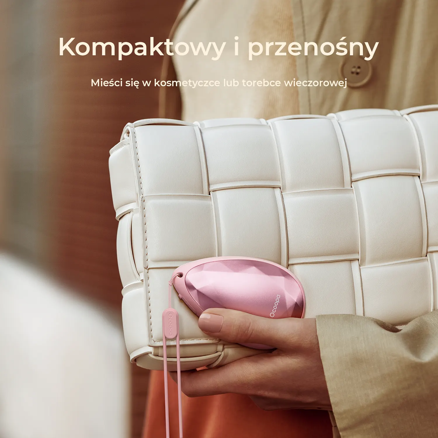 Dłoń trzyma mały, różowy, błyszczący przedmiot przed białą torebką.