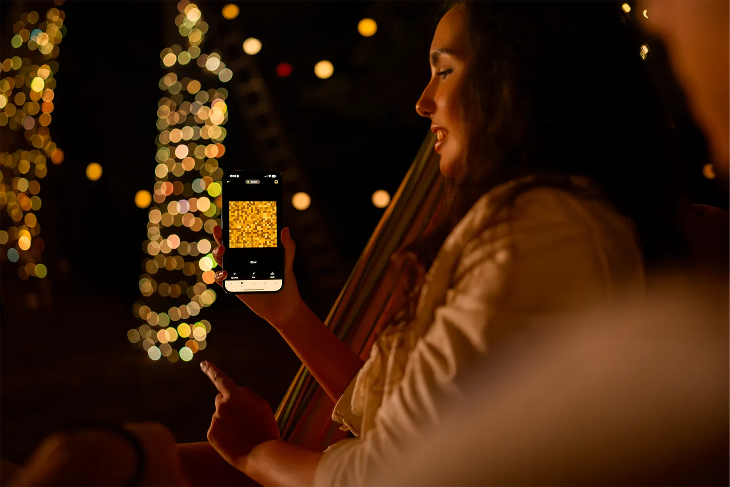 Kobieta trzyma telefon z mozaiką złotych kwadratów, w tle światła bokeh.