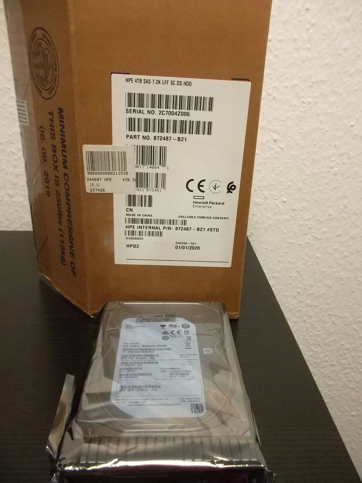 Dysk HPE 4TB SAS w pudełku obok rozpakowanego dysku.