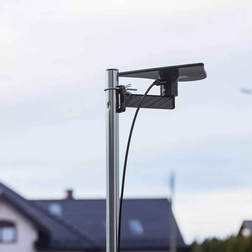 Czarna antena jest przymocowana do metalowego słupa, z domami w tle.
