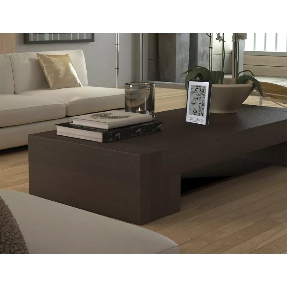 Cyfrowy miernik pogody na ciemnym stoliku kawowym z książkami i świecą.