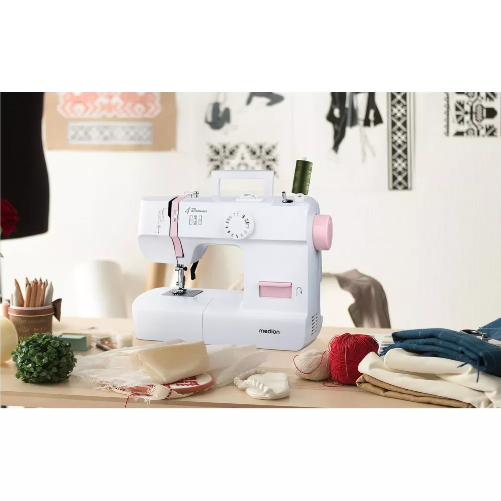 Biała maszyna do szycia z różowymi akcentami, szpulami nici i tkaniną na stole.