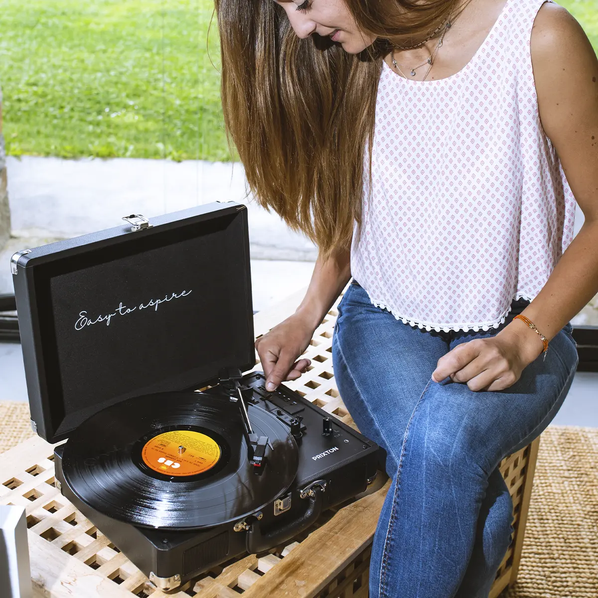 Kobieta z długimi włosami odtwarza płytę na przenośnym gramofonie.