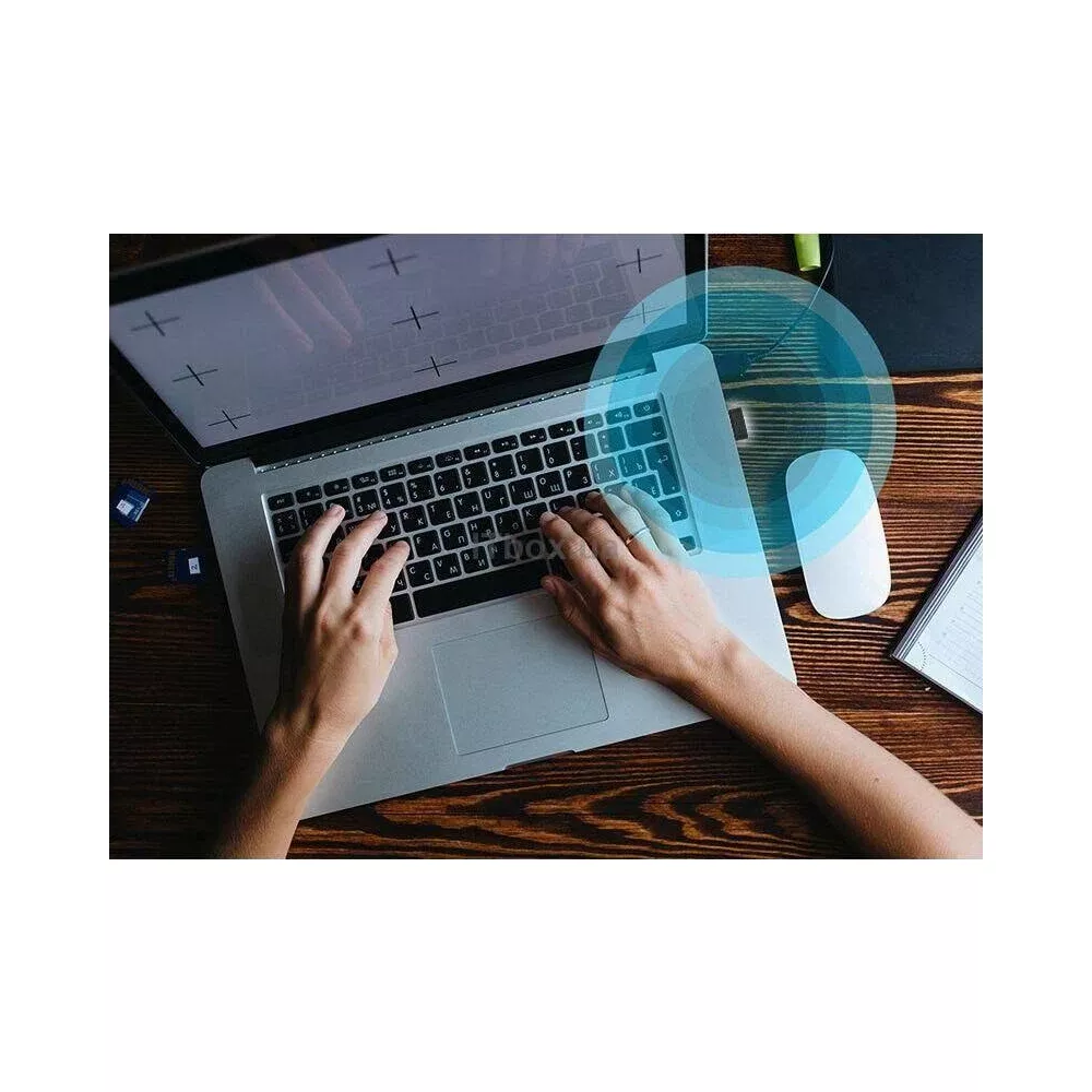 Dłonie piszące na laptopie. Obok na drewnianym biurku leży biała mysz.