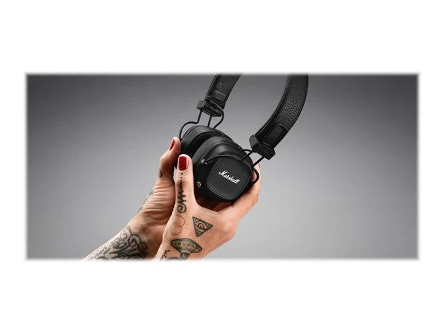 Manos sosteniendo auriculares Marshall negros, con tatuajes.