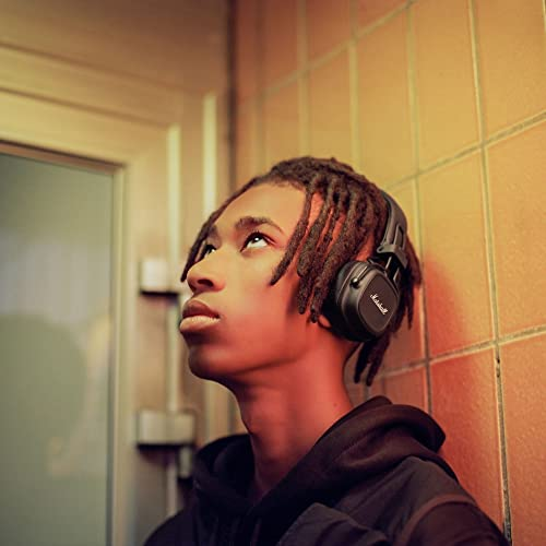 Un joven con auriculares Marshall negros, mirando hacia arriba. Fondo de baldosas color canela.