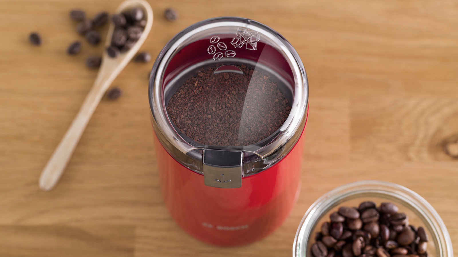 Rote Kaffeemühle mit gemahlenem Kaffee, Bohnen und einem Löffel.