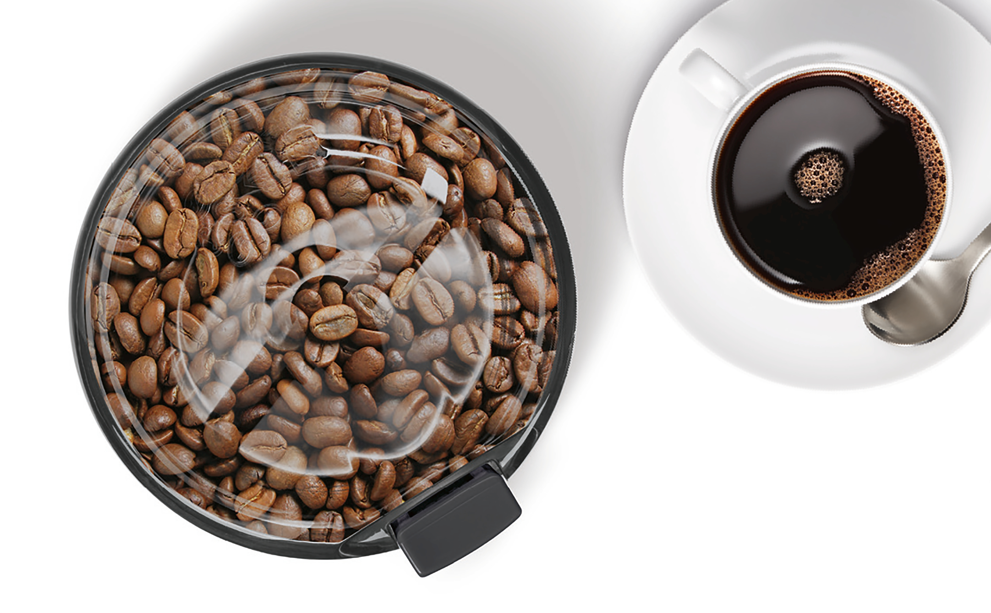 Draufsicht auf Kaffeebohnen in einer Mühle und eine Tasse Kaffee.
