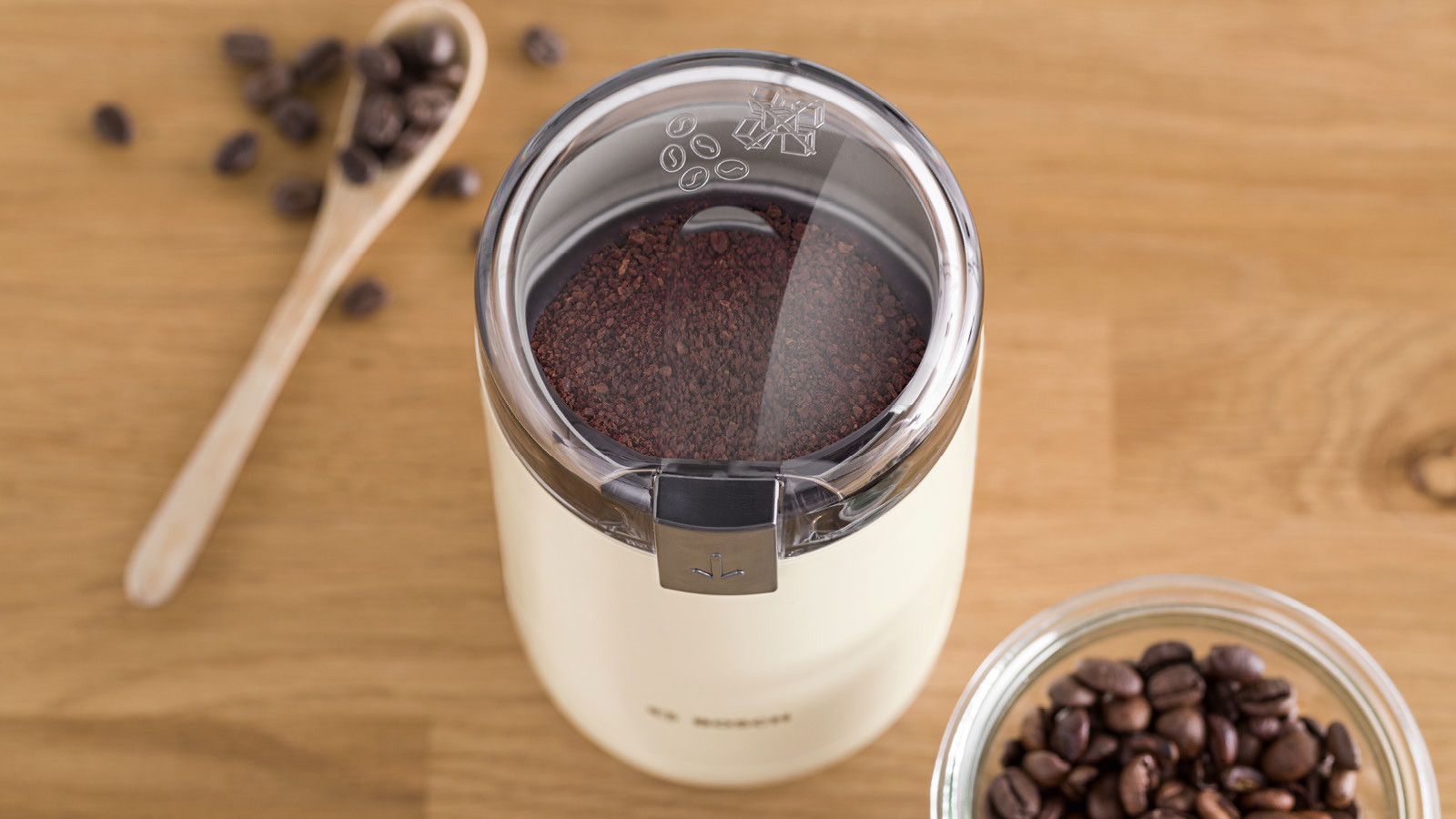 Kaffeemühle mit gemahlenem Kaffee, Holzlöffel und Kaffeebohnen.