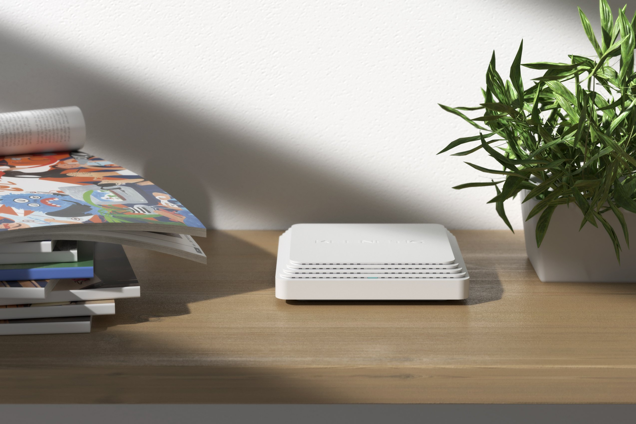 Weißer Router auf Holztisch. Magazin und Pflanze befinden sich links bzw. rechts.