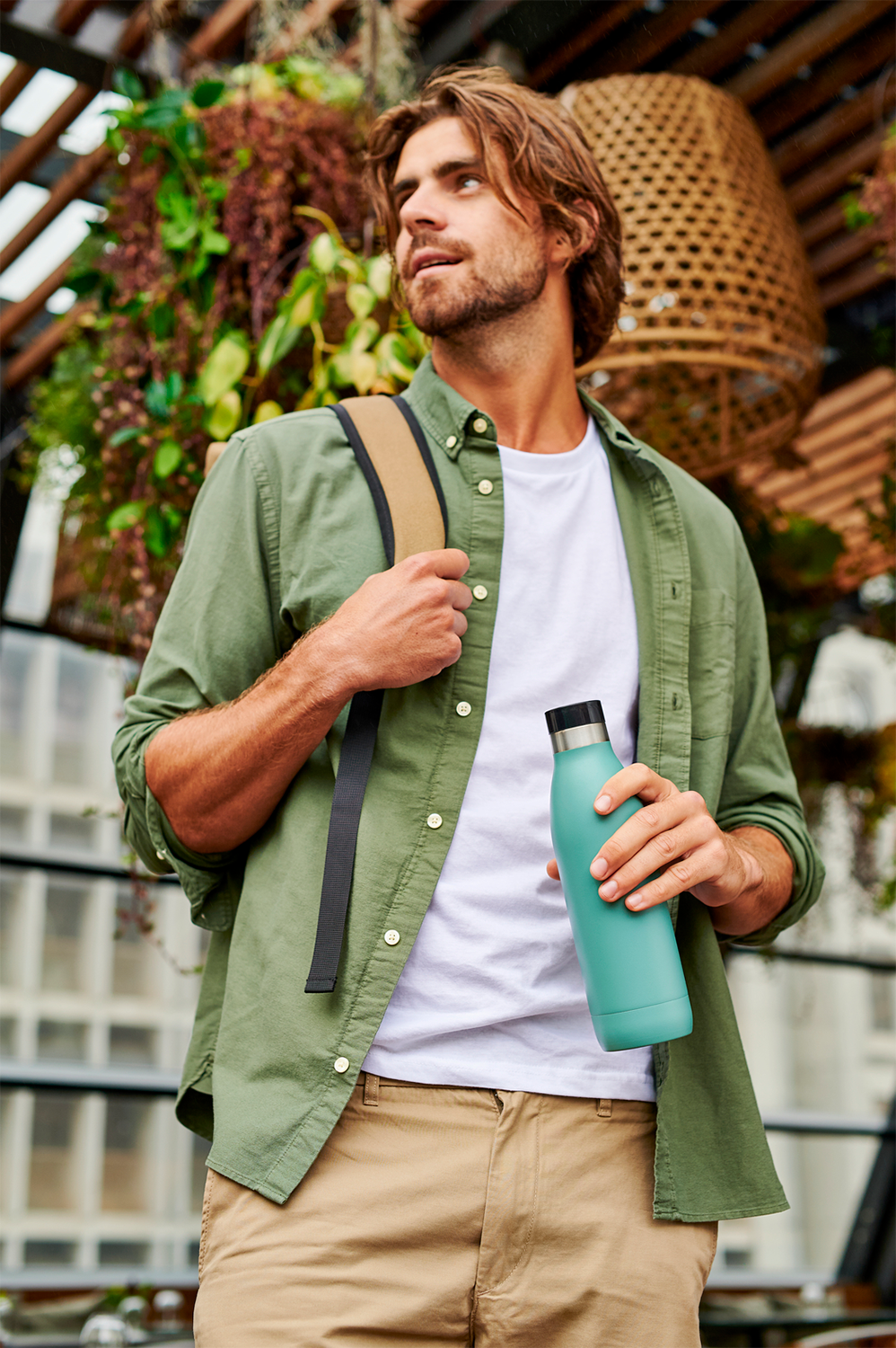 Man buiten met een turquoise waterfles, groen overhemd en beige broek.