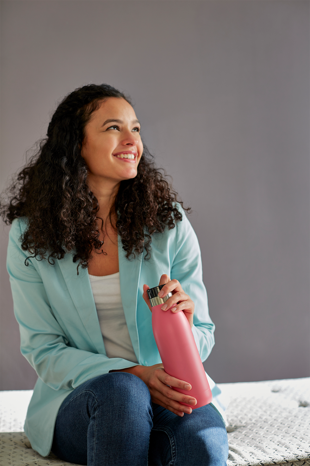 Smiling woman holding a pink water bottle, looking upwards.
