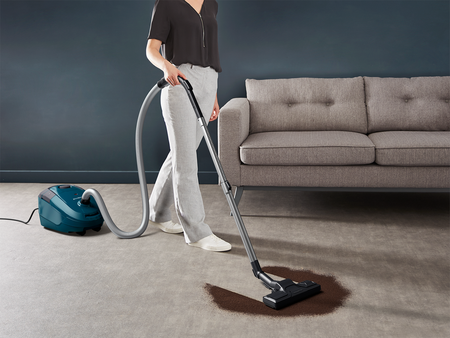 Woman vacuuming a carpet in a living room with a couch in the background.