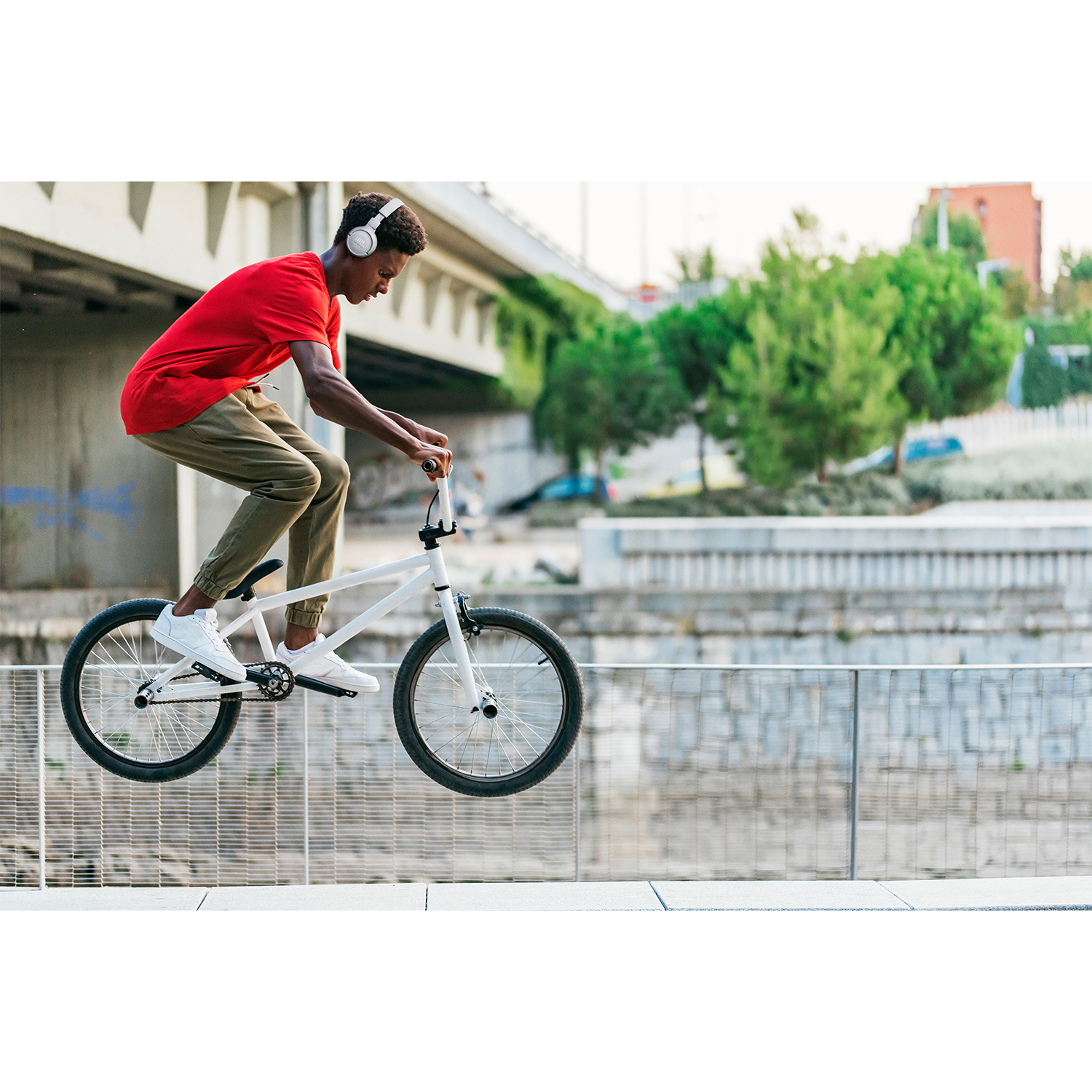 Uomo che guida una bici BMX bianca saltando una recinzione metallica. Sfondo urbano.