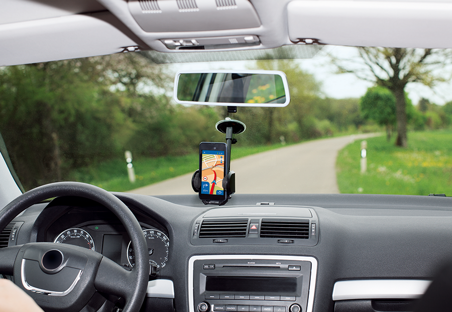 A car interior with a phone mounted on the dashboard displaying a navigation app. A road is visible outside.