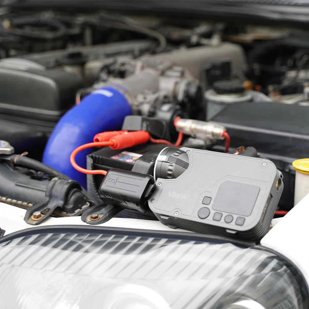 Compartiment moteur avec batterie, câbles de démarrage et un appareil de charge connecté.
