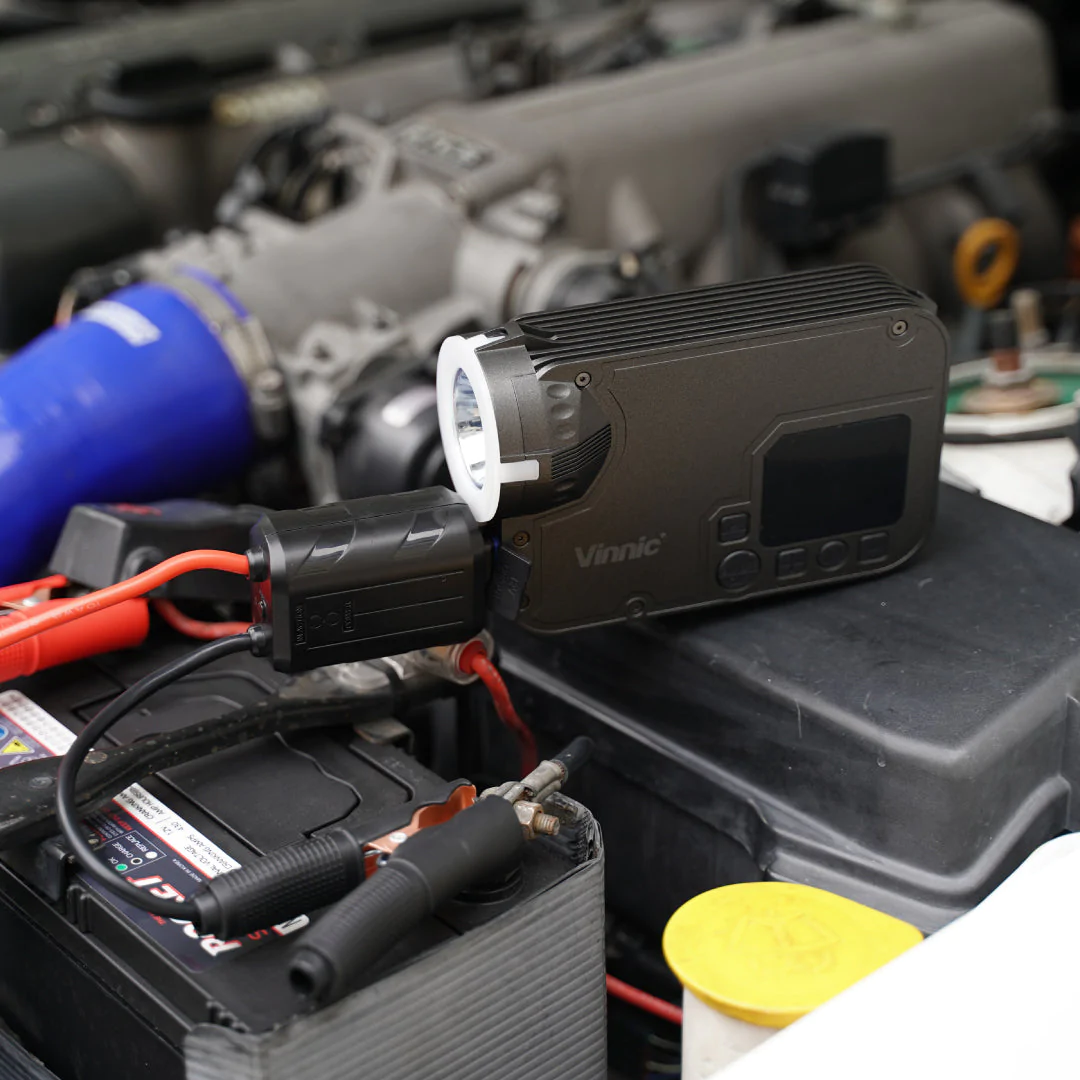 Un compartiment moteur de voiture avec un appareil noir et des câbles de démarrage attachés.