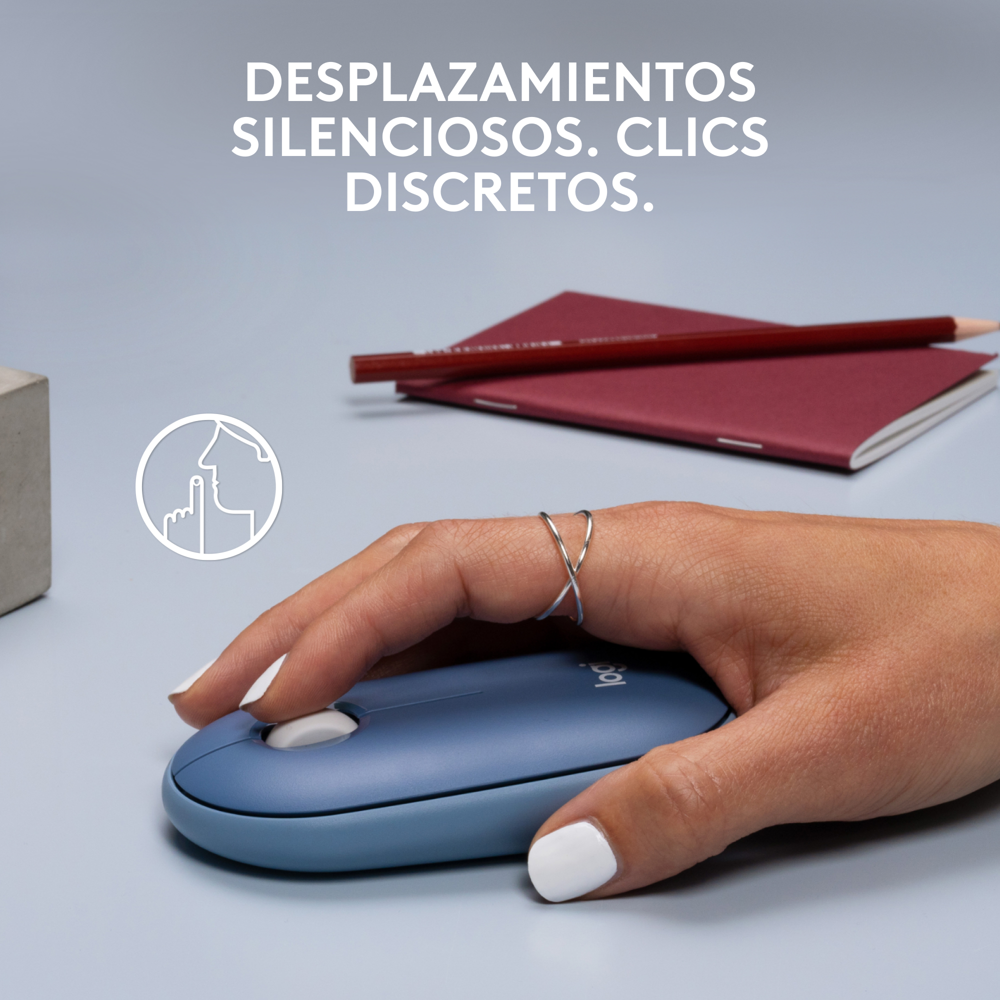 Una mano usa un ratón Logitech azul sobre una superficie gris. El texto dice 'CLICS SILENCIOSOS. CLICS DISCRETOS'.