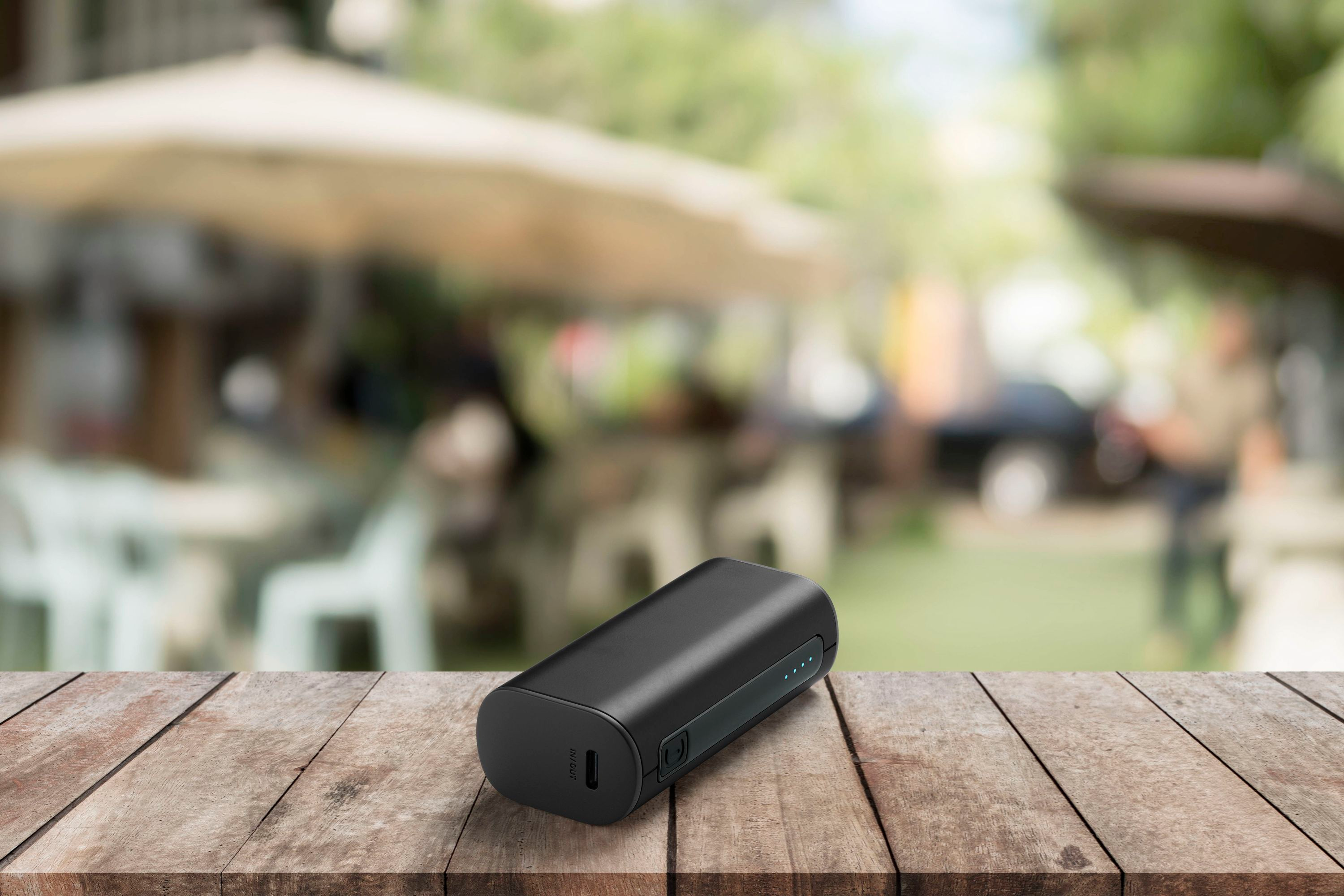Schwarze Powerbank auf Holztisch, unscharfe Szene im Hintergrund.