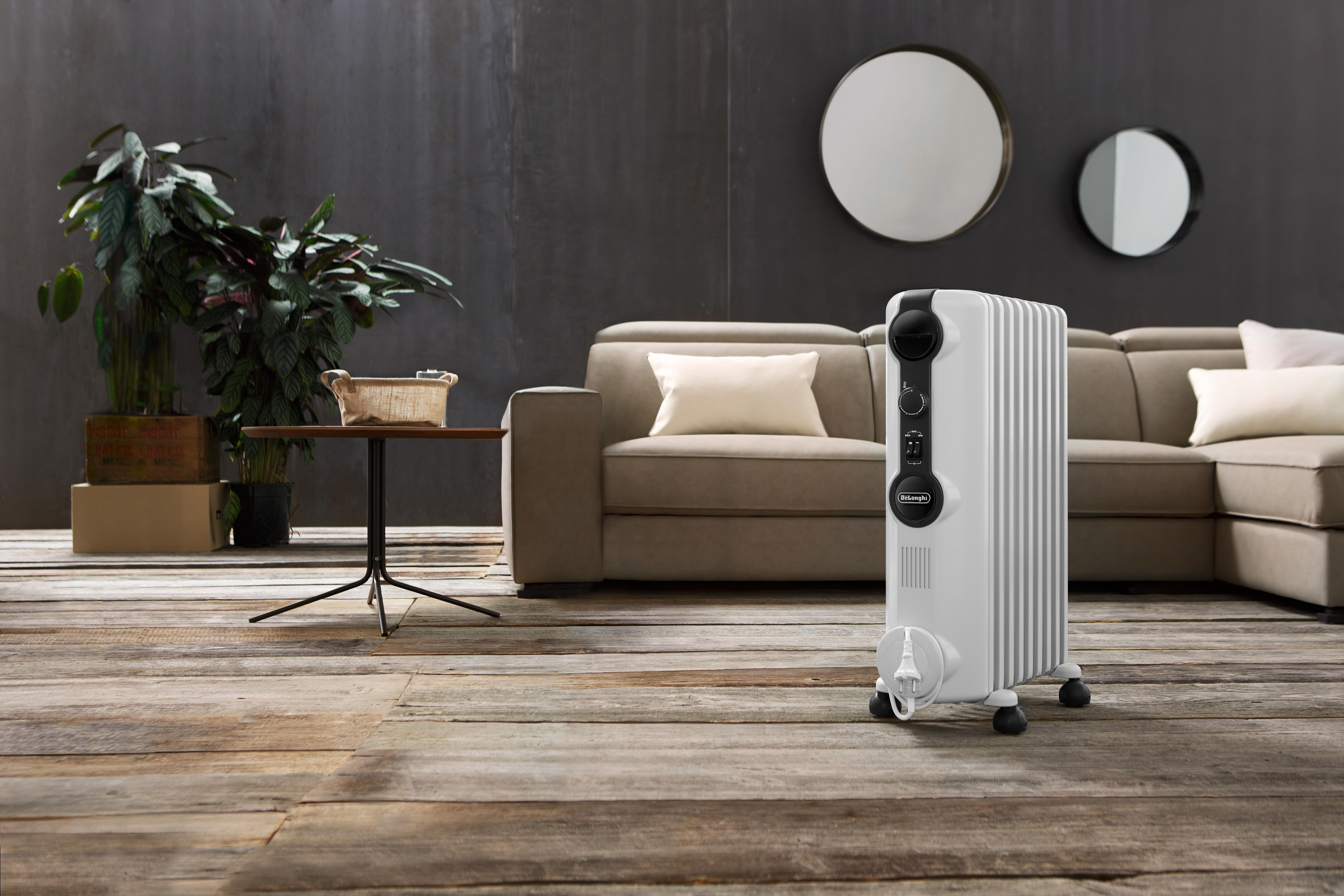 Weiß-grauer Ölradiator, mit Sofa und Pflanzen im Hintergrund.