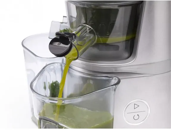 A juicer dispenses green juice into a clear container.